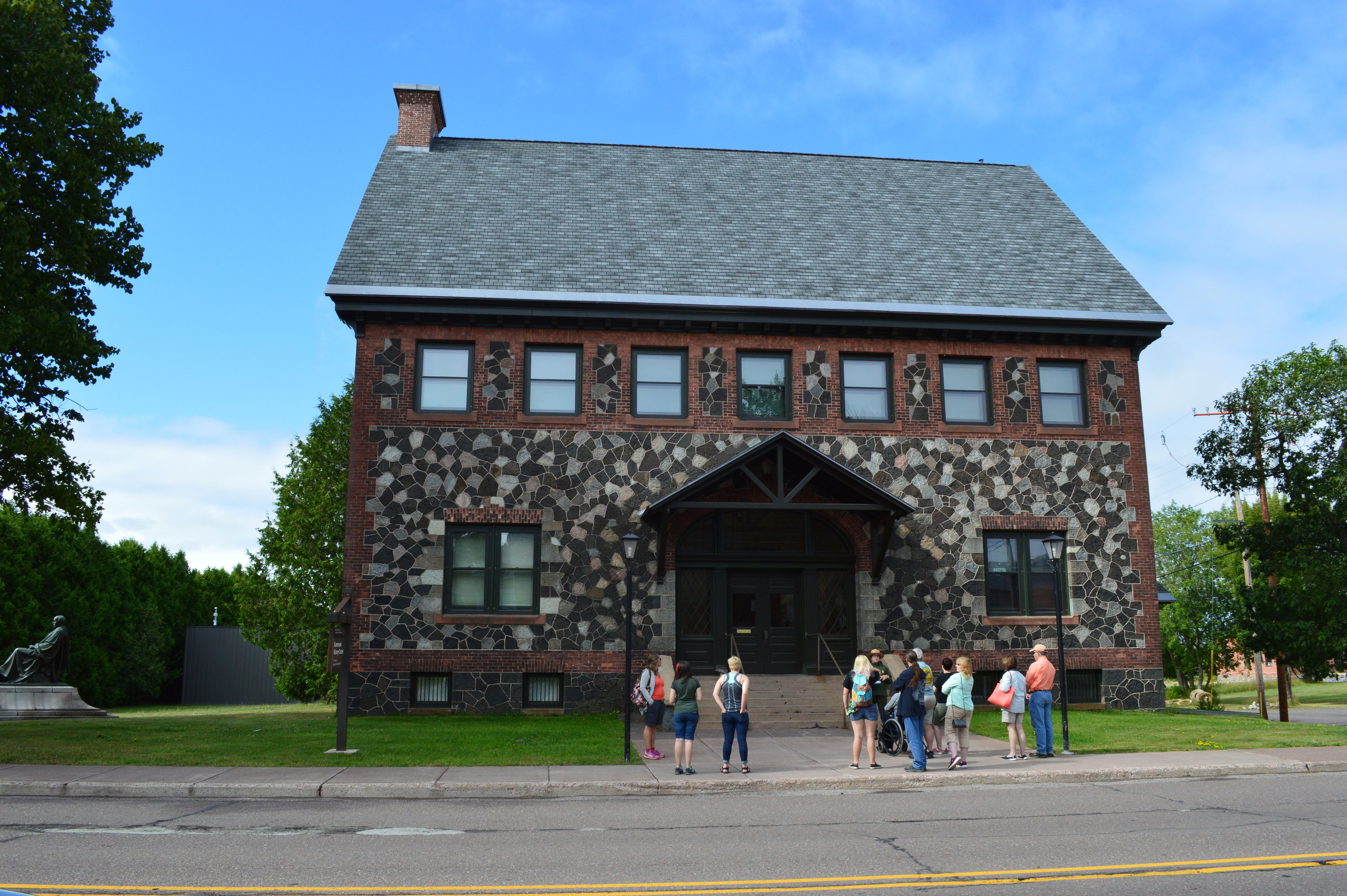 Two story stone and brick building. a ranger leads a group of visitors in front or the steps