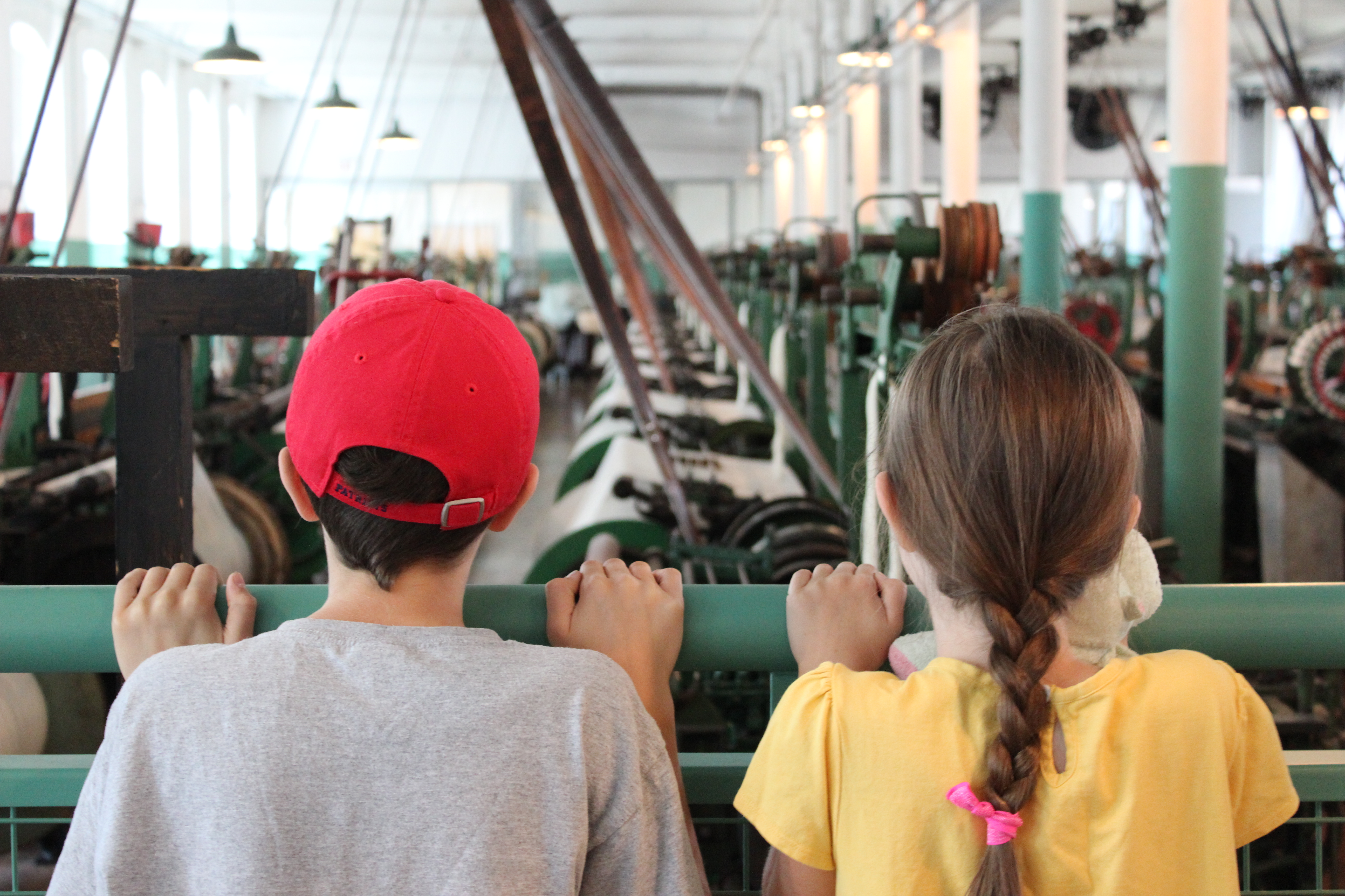 Two young visitors look over the rail at a room full of working looms