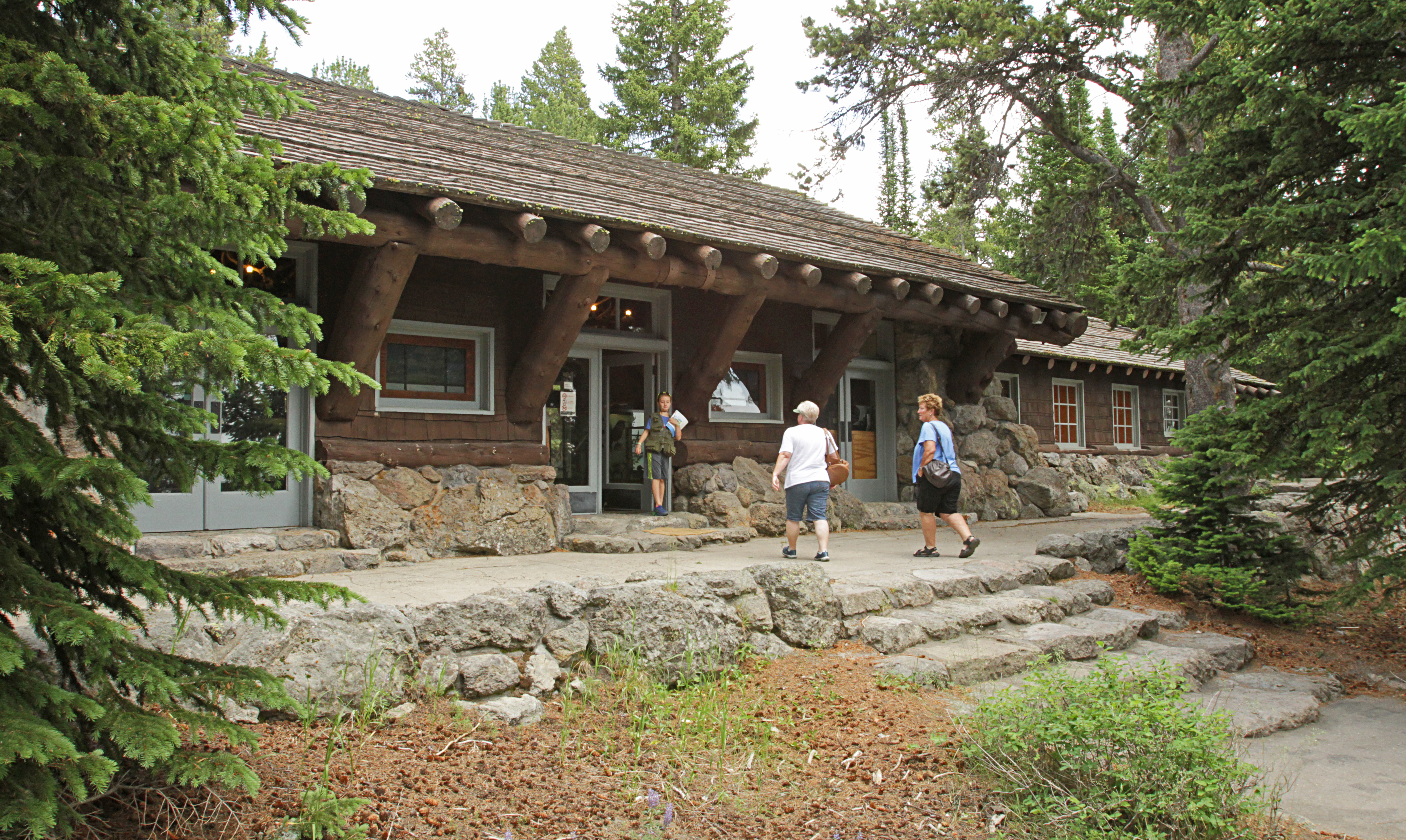 Visitors walk into a rustic, log and stone building.