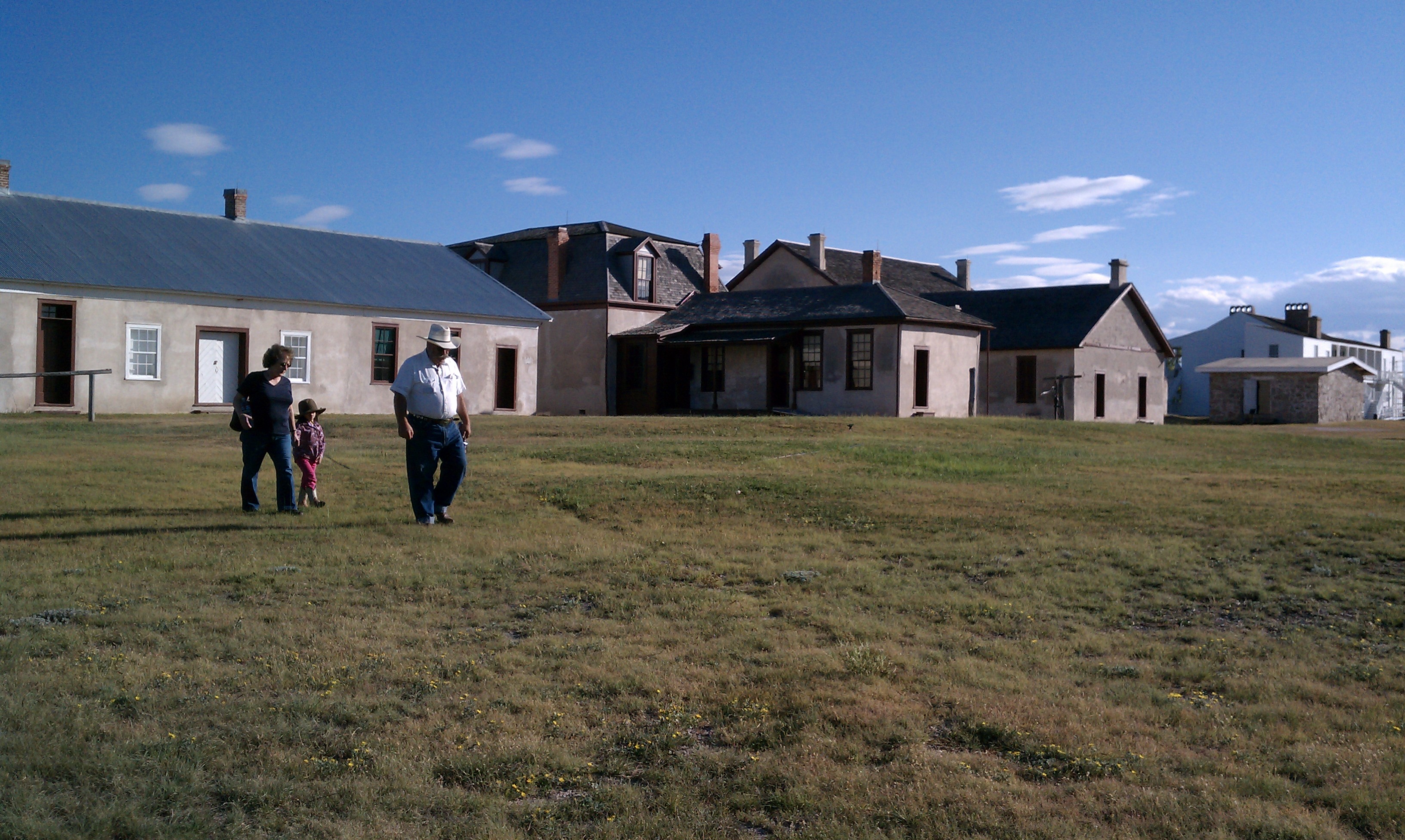 Two people walk on a green lawn in front of historic fort buildings.