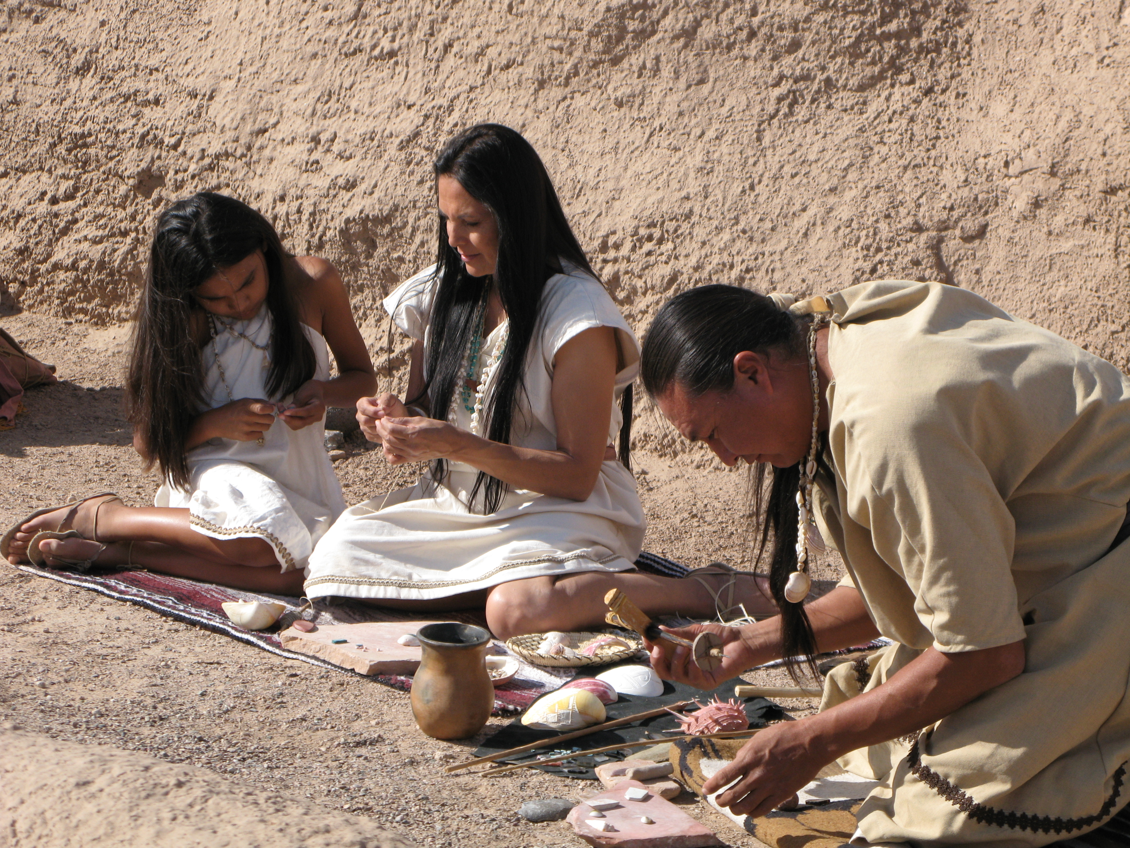 child, adult female, adult male American Indian actors in costume making jewelry in movie shoot