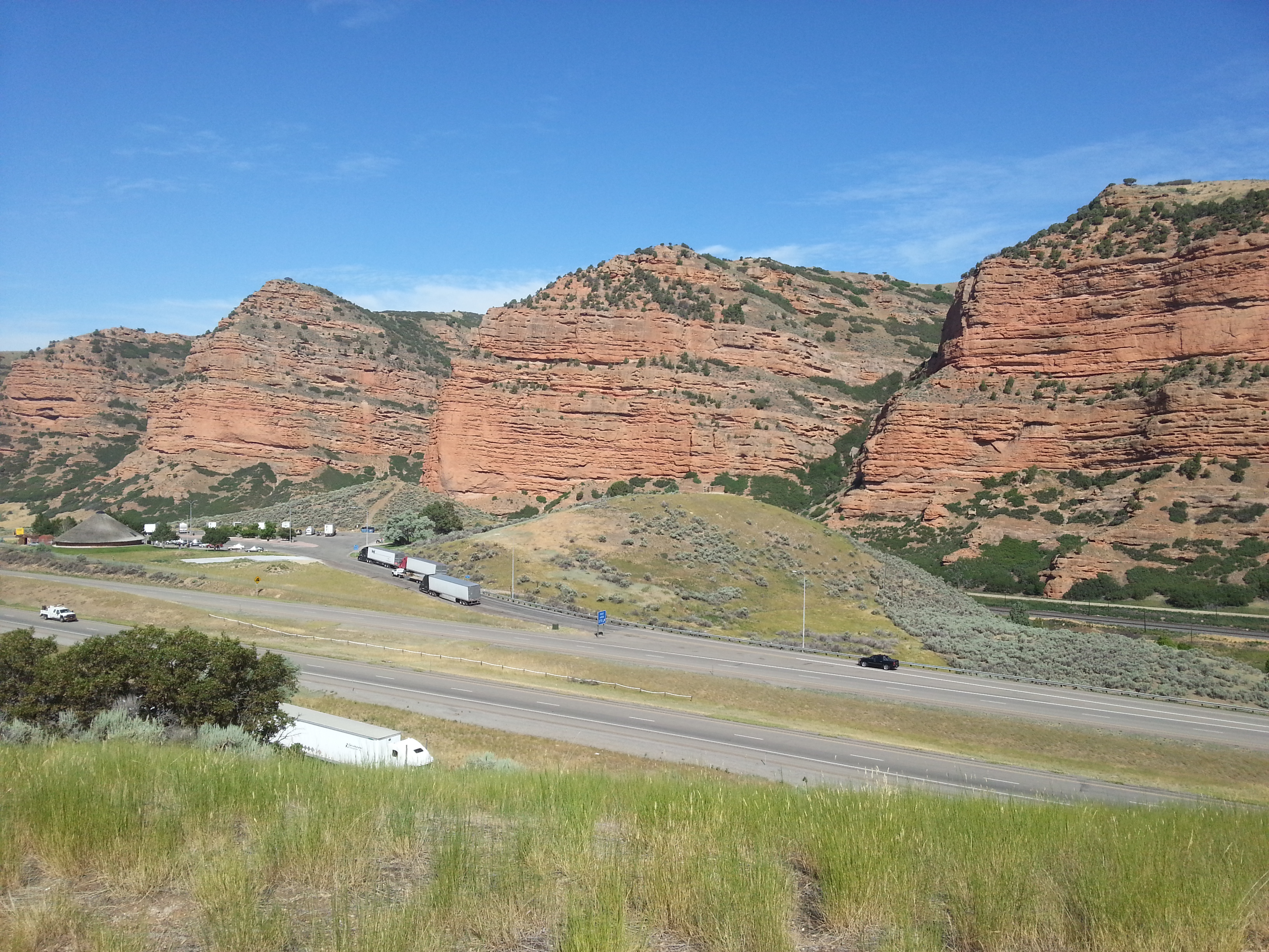 Red cliffs line a highway as seen from a high point with grass in the foreground.