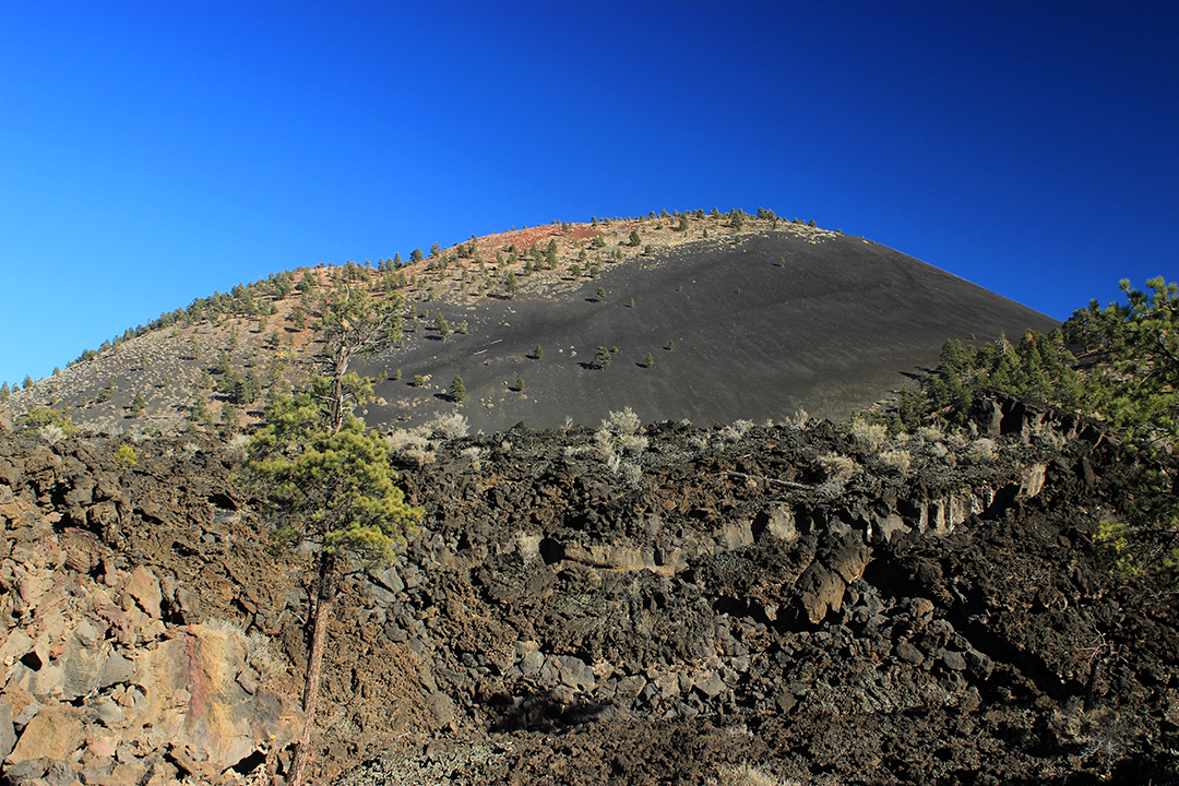 a jagged field of lava beneath a cinder cone volcano