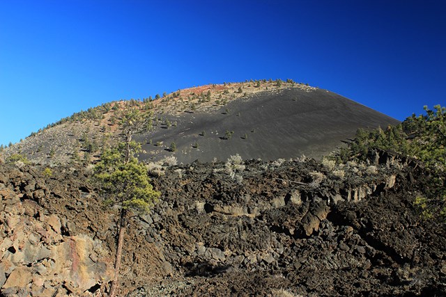 a jagged field of lava beneath a cinder cone volcano