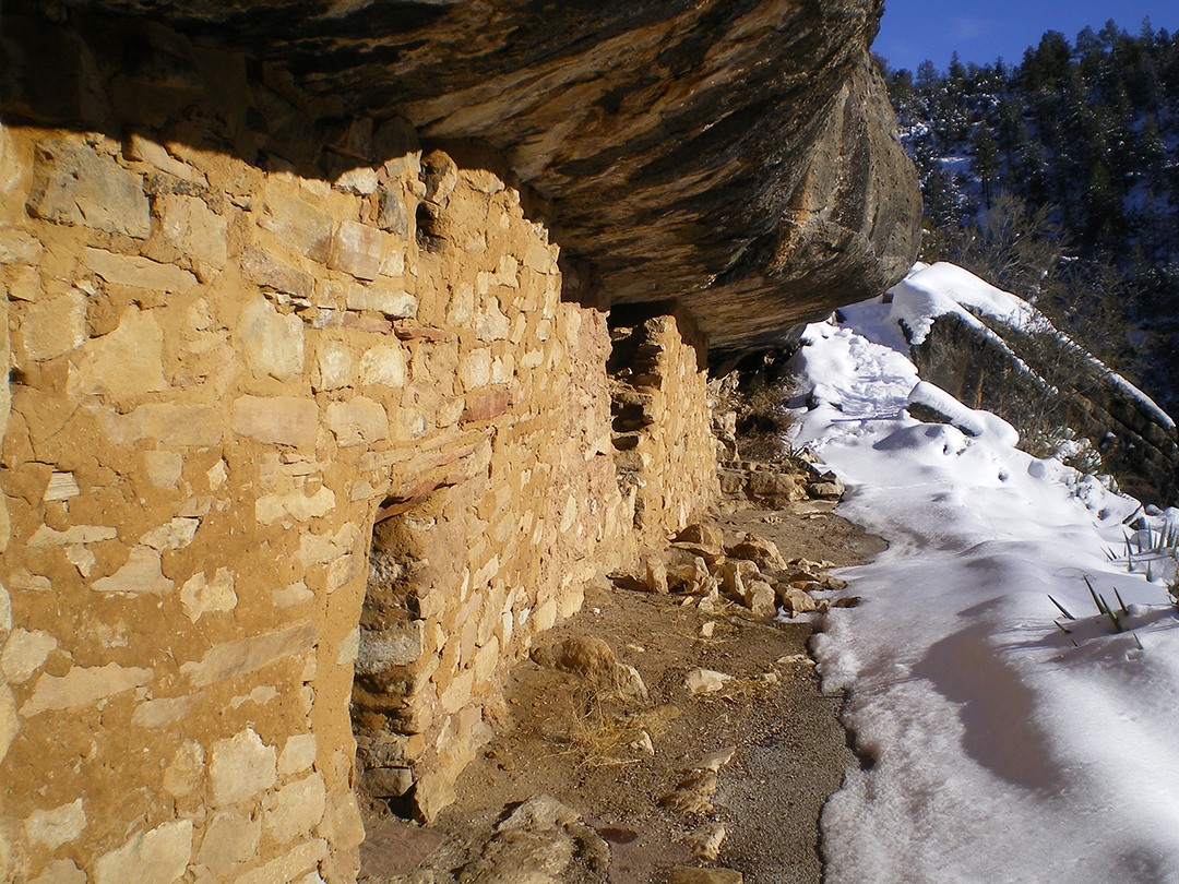 warm sunlight illuminates a cliff dwelling wall beside a snowy trail