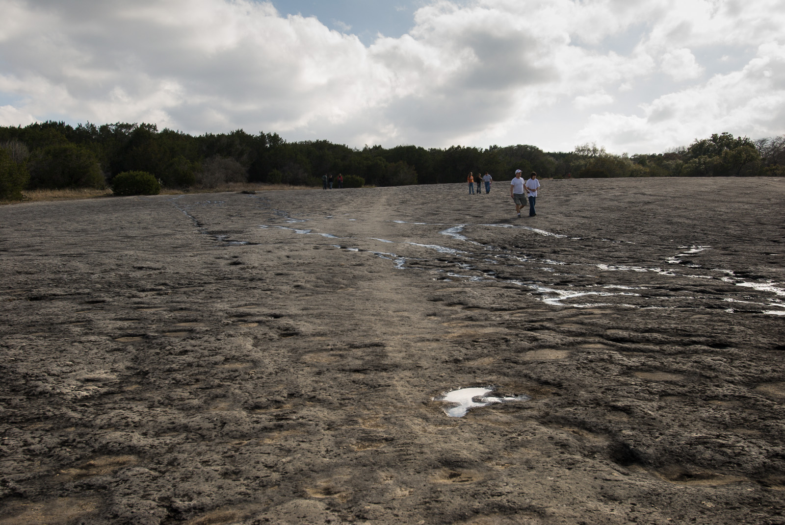 rock indentations in a dry creek with five people walking under clouds