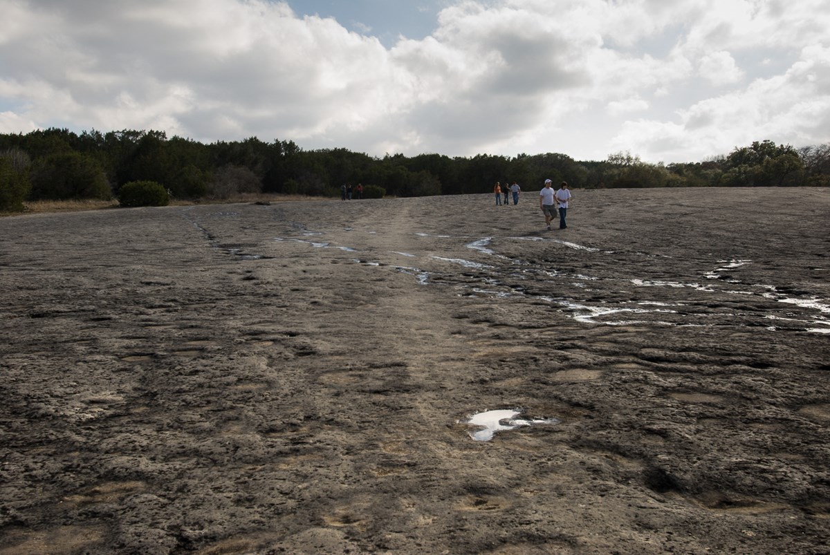 rock indentations in a dry creek with five people walking under clouds