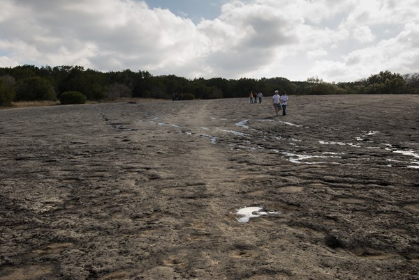 rock indentations in a dry creek with five people walking under clouds