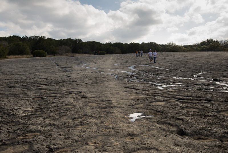 rock indentations in a dry creek with five people walking under clouds