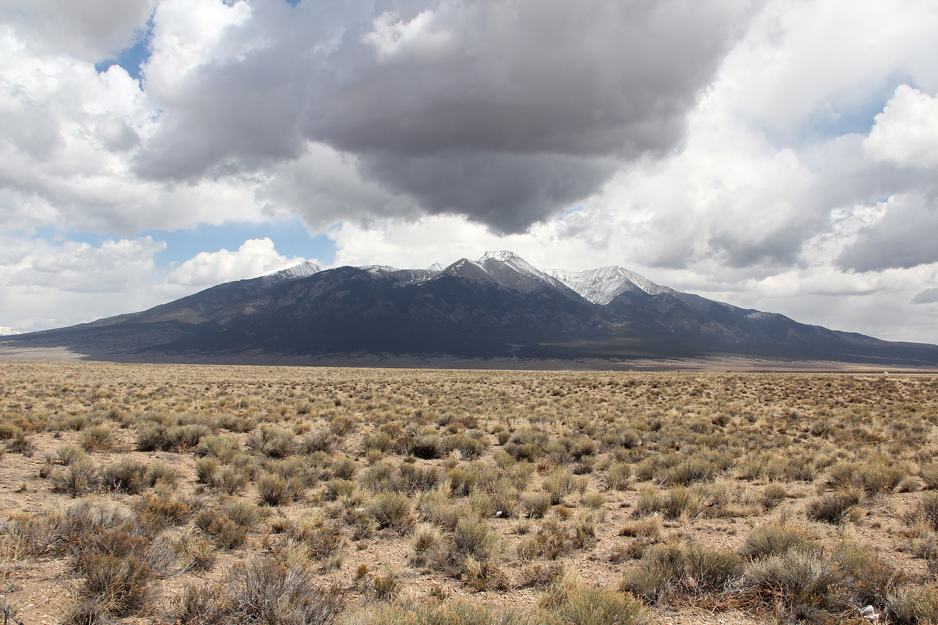 desert scrub in foreground, spiky mountains in background, clouds