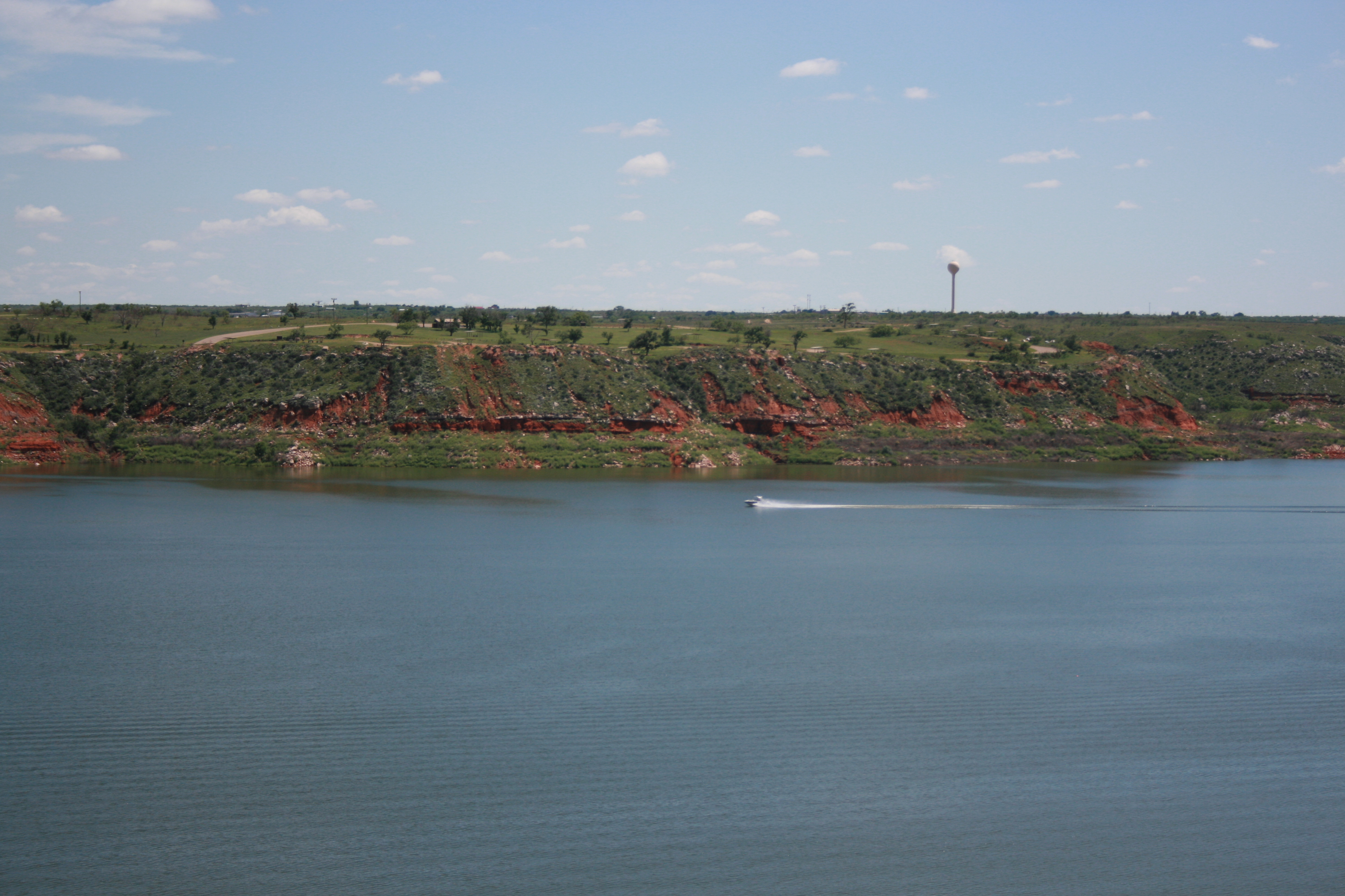 A boat travels across Lake Meredith on a sunny day.  The lake is light blue.