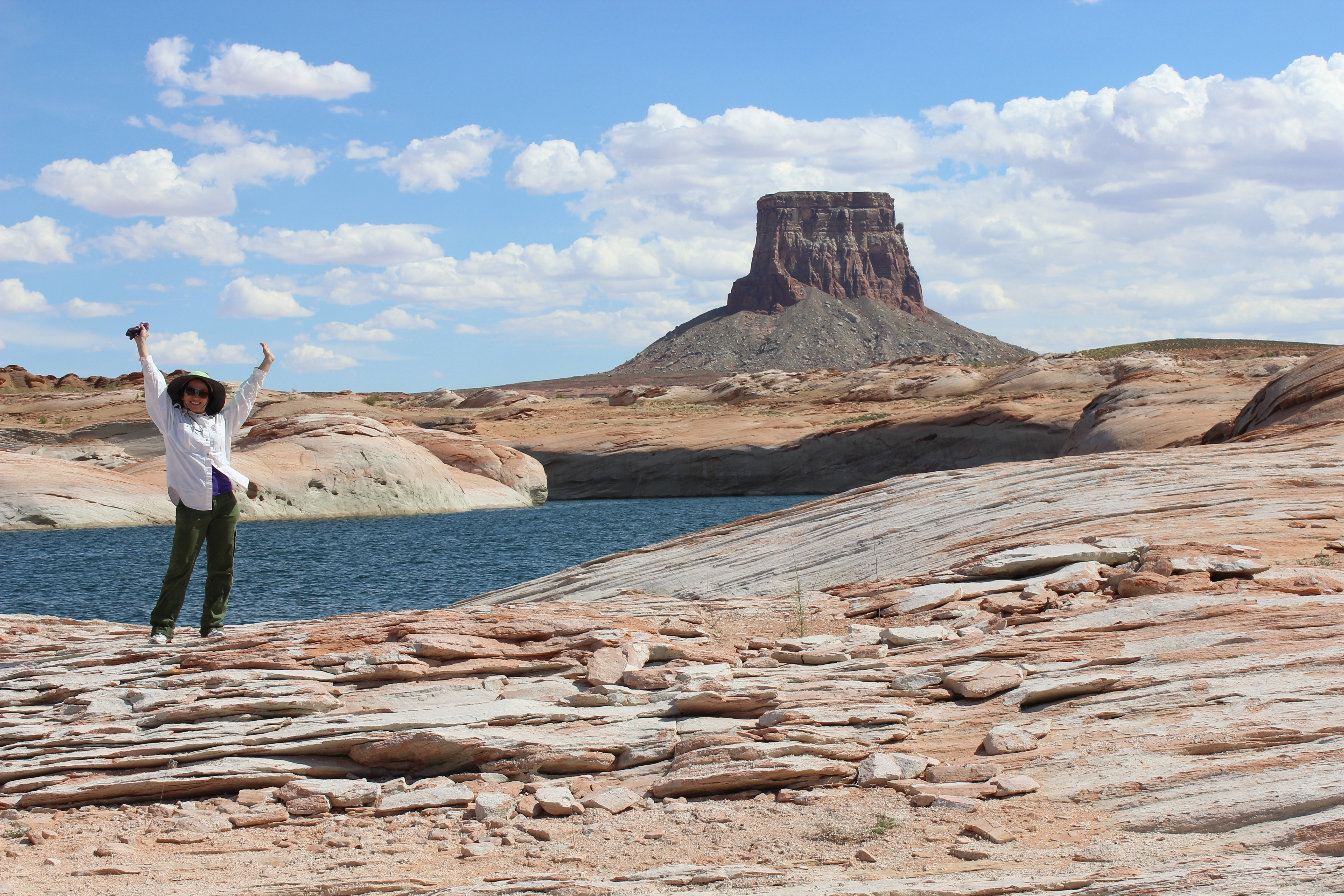 Woman raises her arms while standing in front of a sandstone butte