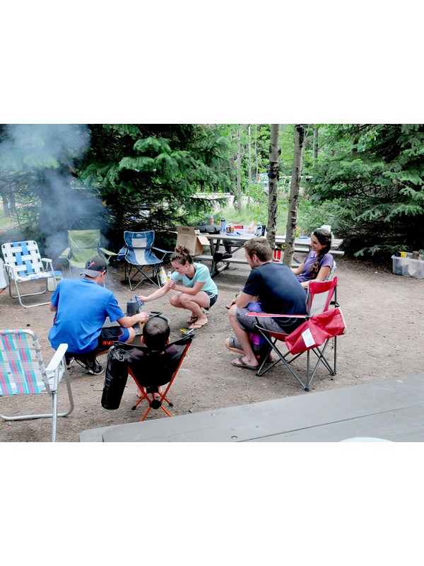 five campers around campfire at campsite