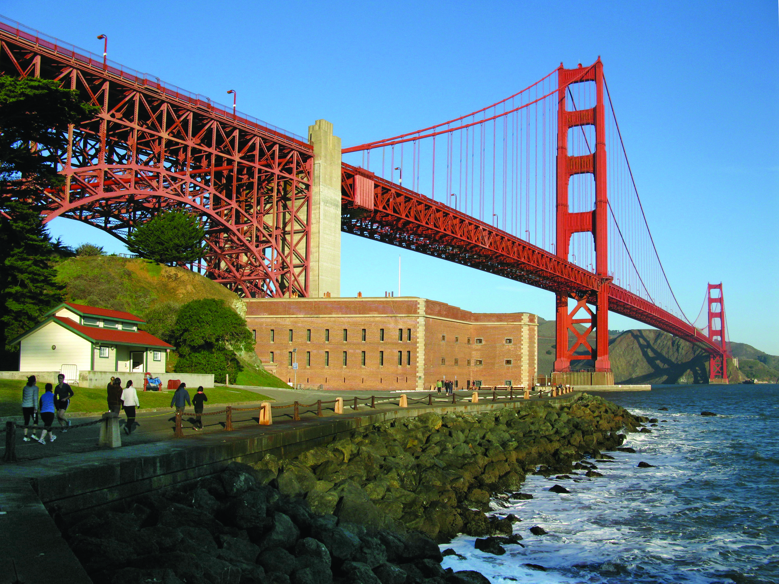 Fort Point with visitors approaching on road in front and Golden Gate Bridge above.