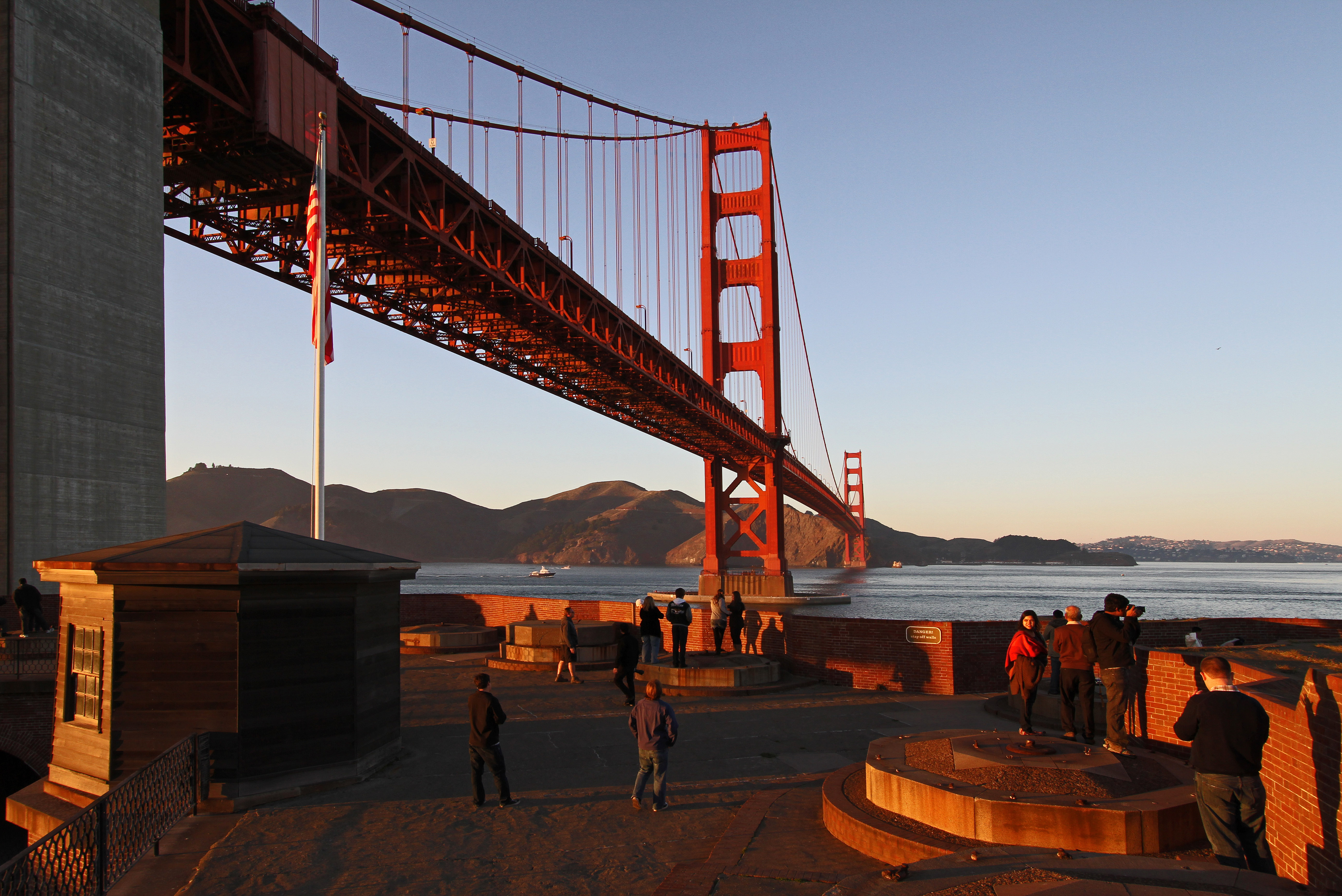 Golden sunset light on the roof of Fort Point with Golden Gate Bridge and bay behind.