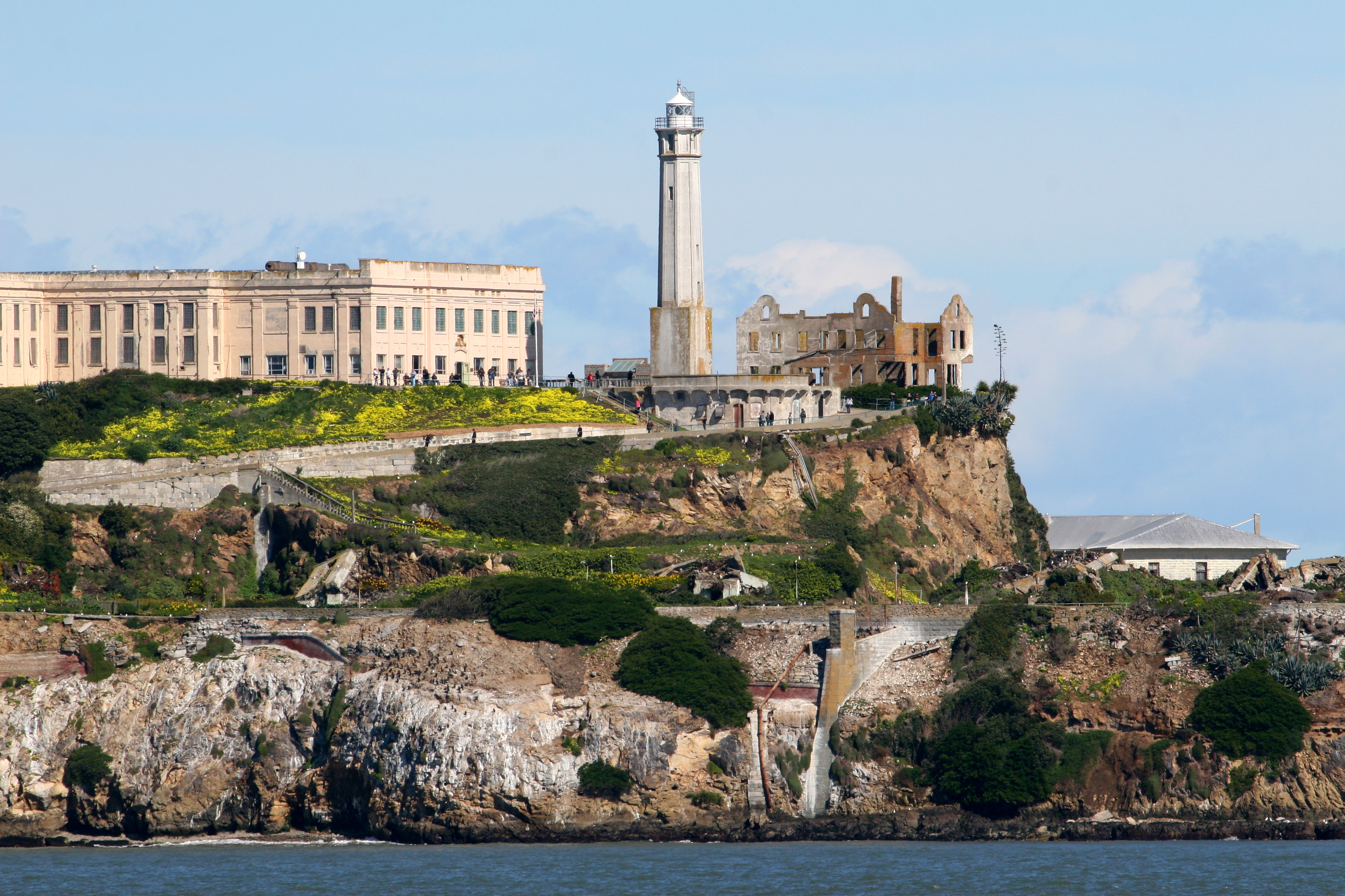 Closeup shot of Alcatraz Island showing lighthouse and prison with yellow flowers on slope in front.