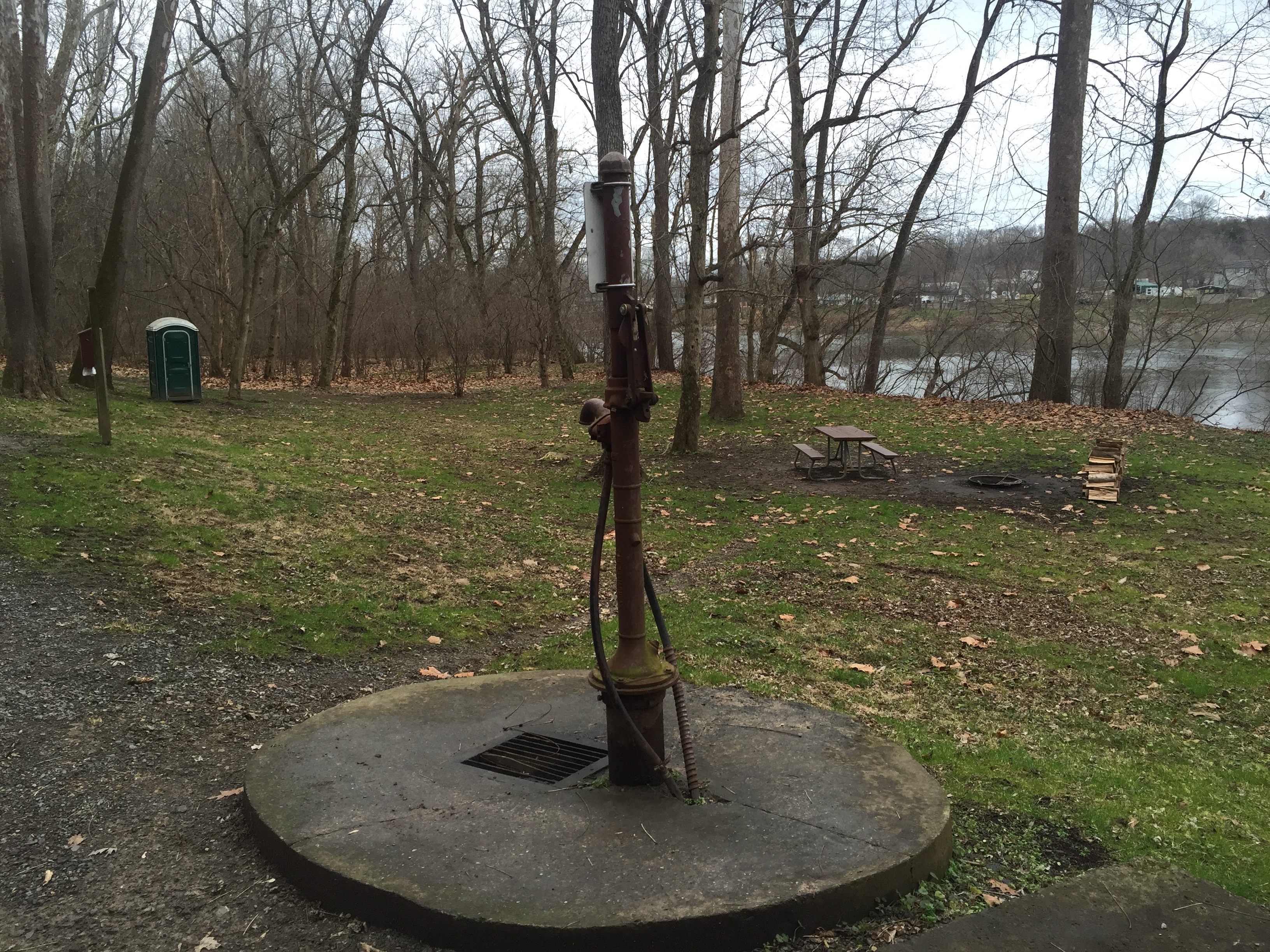 A water pump is seen in the foreground of the open grassy campsite area.