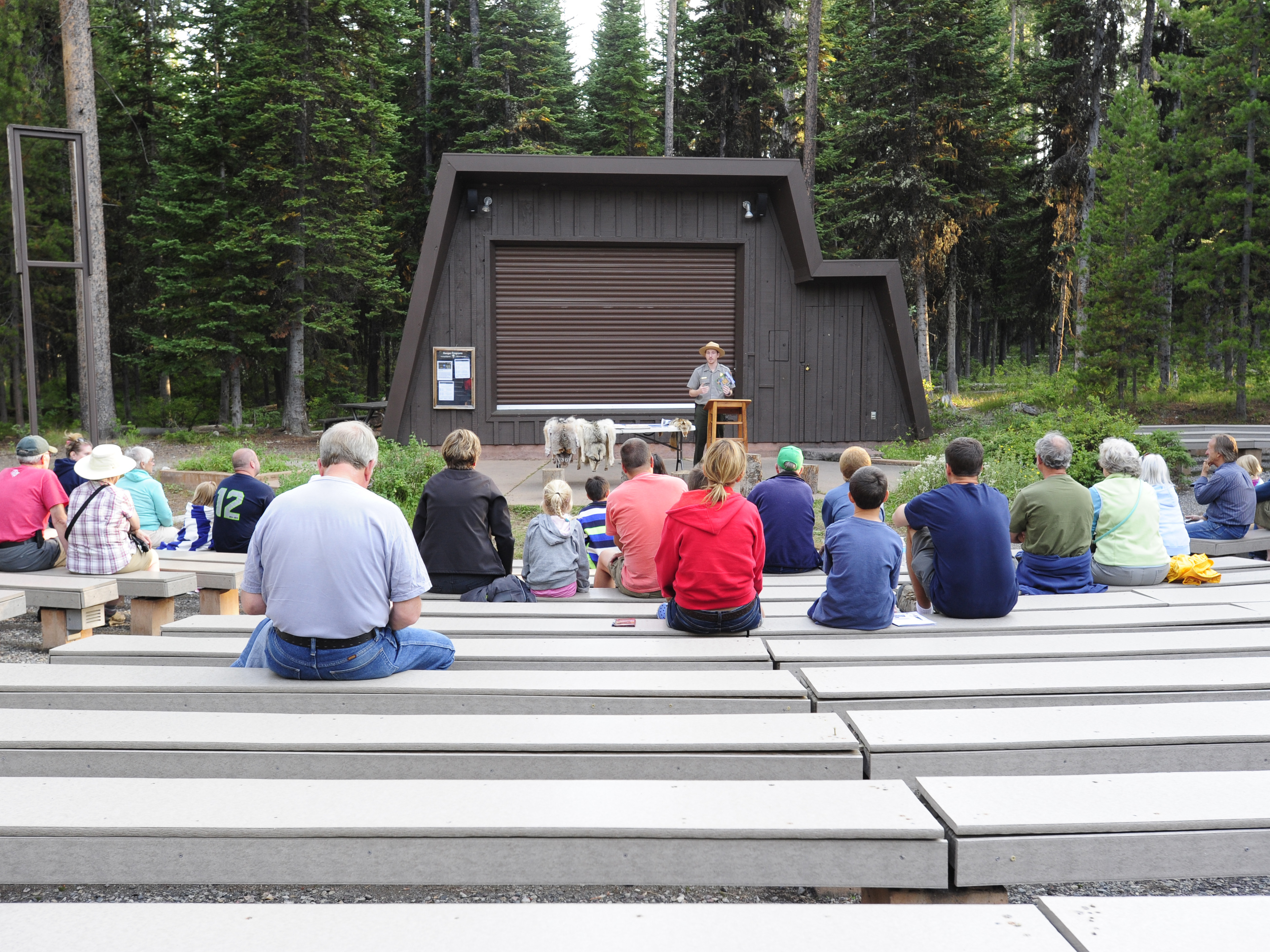 outside amphitheater with visitors sitting on benches and a ranger on stage making a presentation