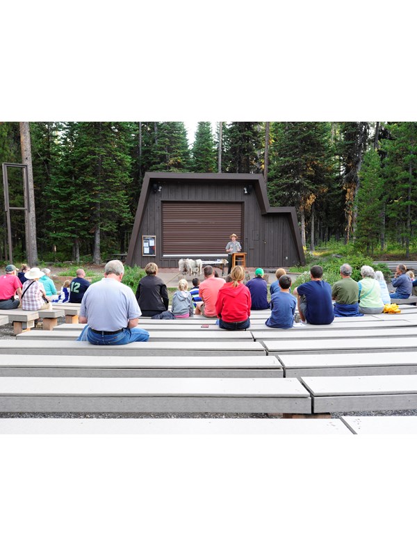 outside amphitheater with visitors sitting on benches and a ranger on stage making a presentation