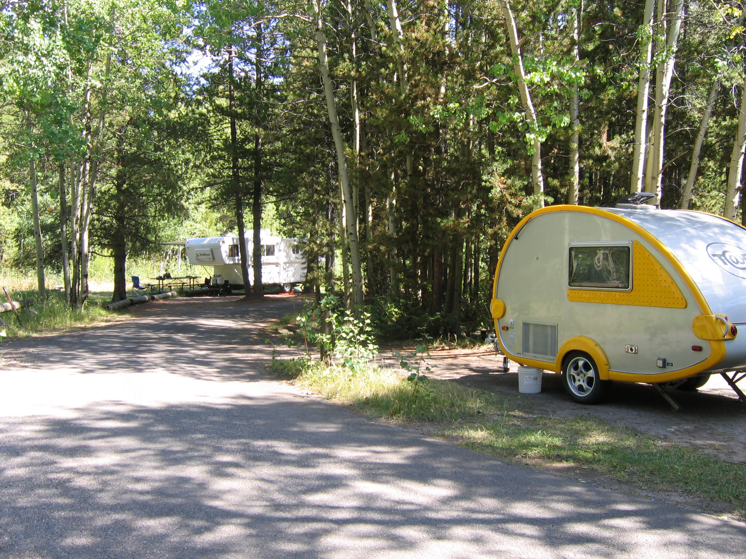 two small white trailers at campsites with conifers surrounding them