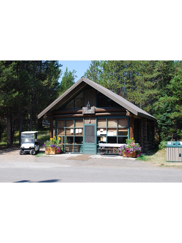 RV park brown log cabin with green door and flowers in barrels