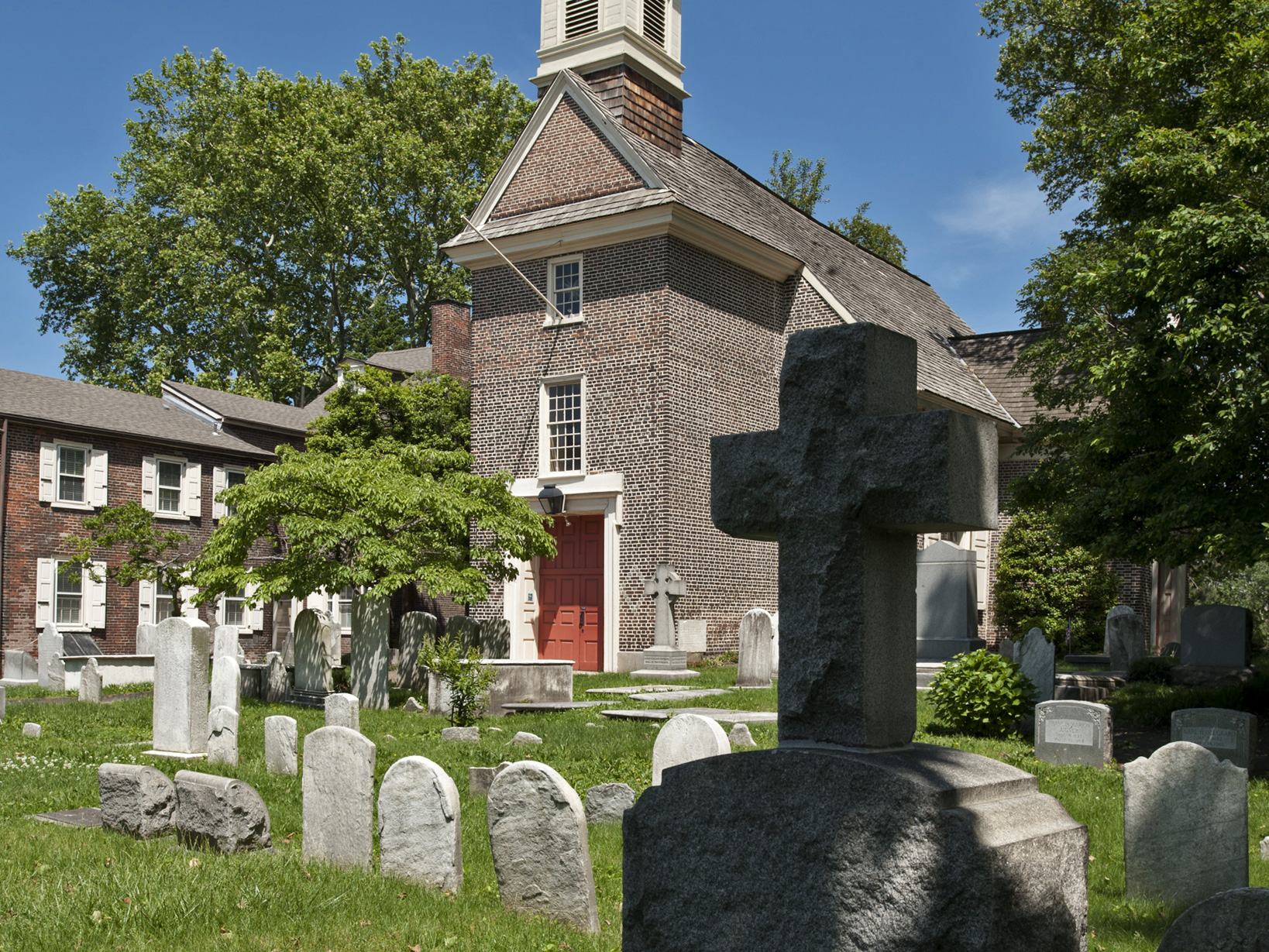 A color photo of the Gloria Dei Church yard showing tombstones with the church in the background.