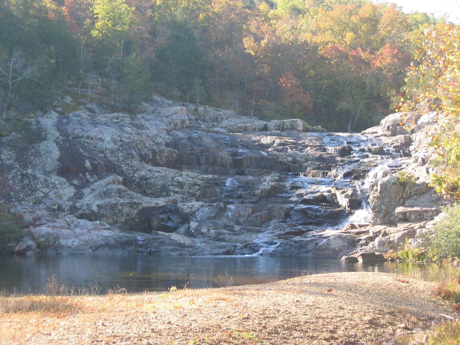 a brown gravel bar with distant waterfall of water flowing down over brown rocks