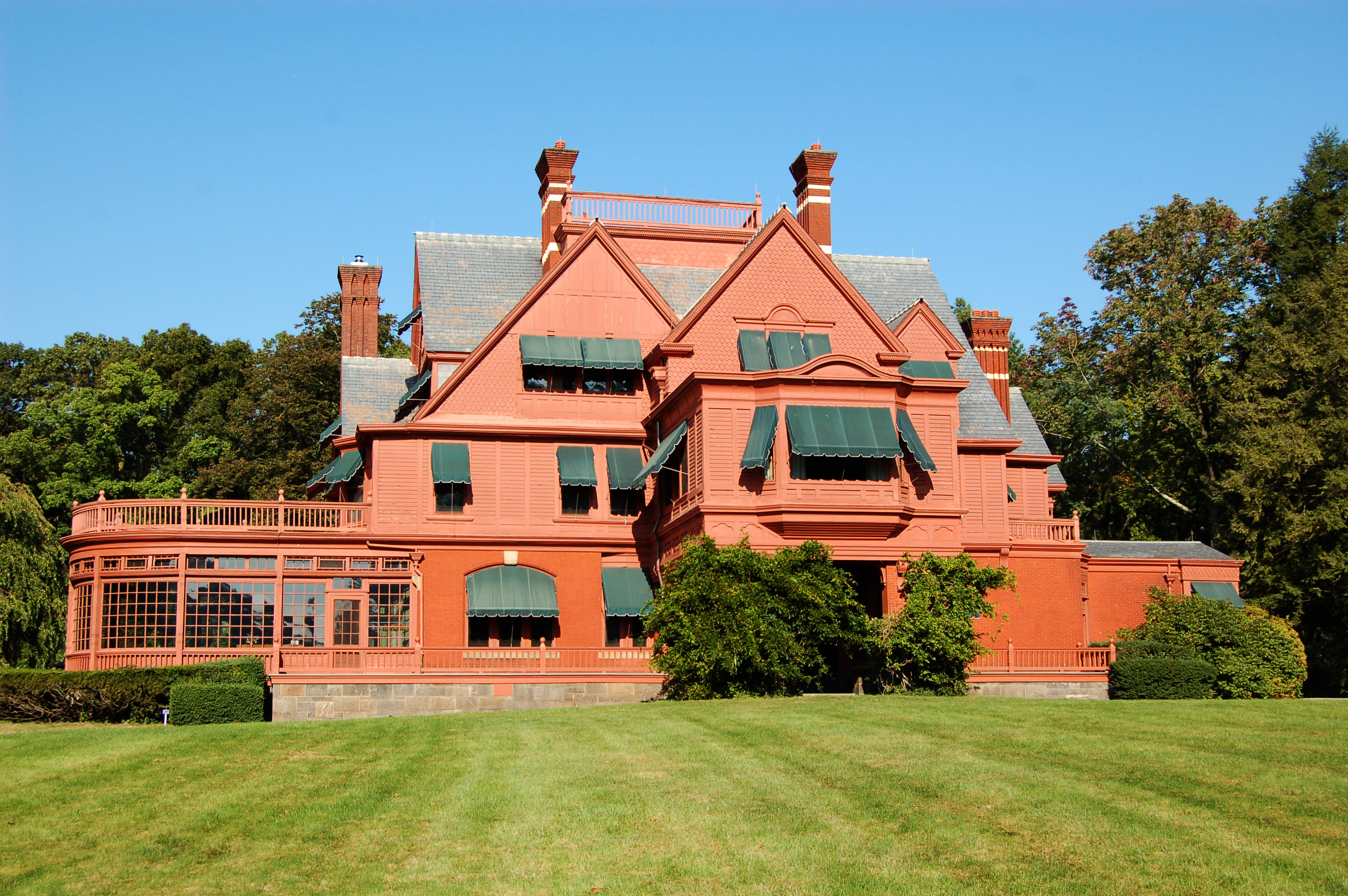 Large salmon colored Victorian mansion with green lawn and blue sky