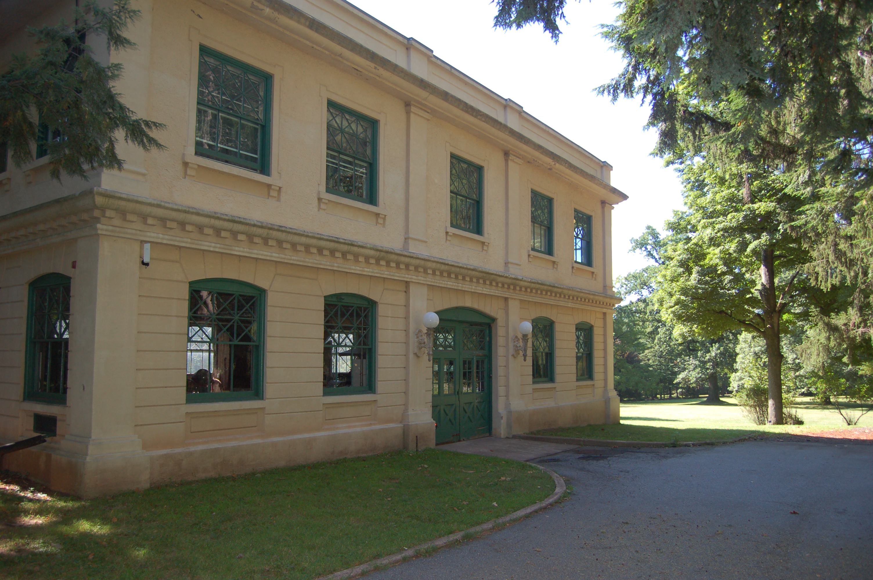 Cream colored, two story cement building surrounded by large trees