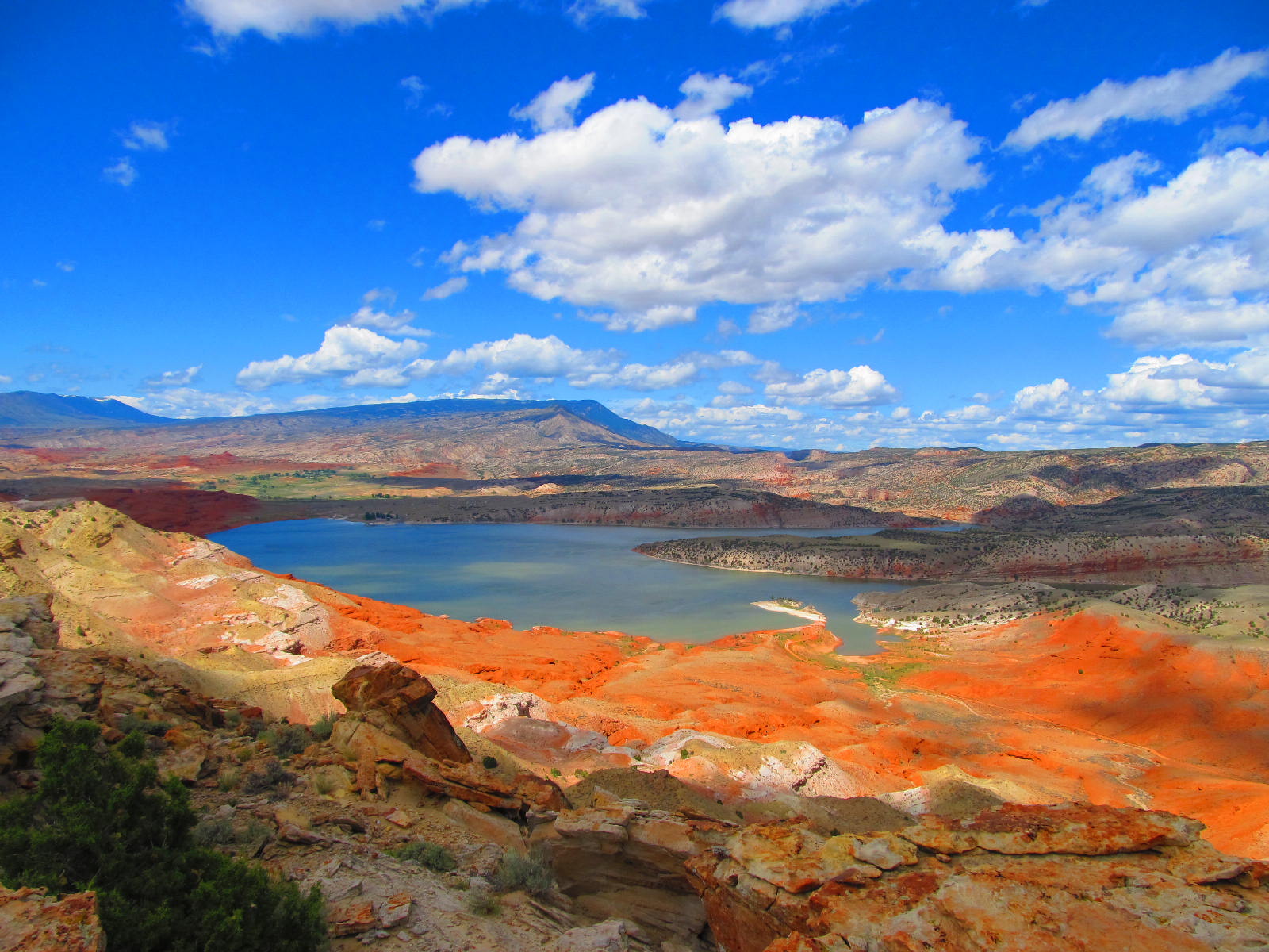 Red hills in the foreground with Bighorn Lake in the background with a brilliant blue sky.