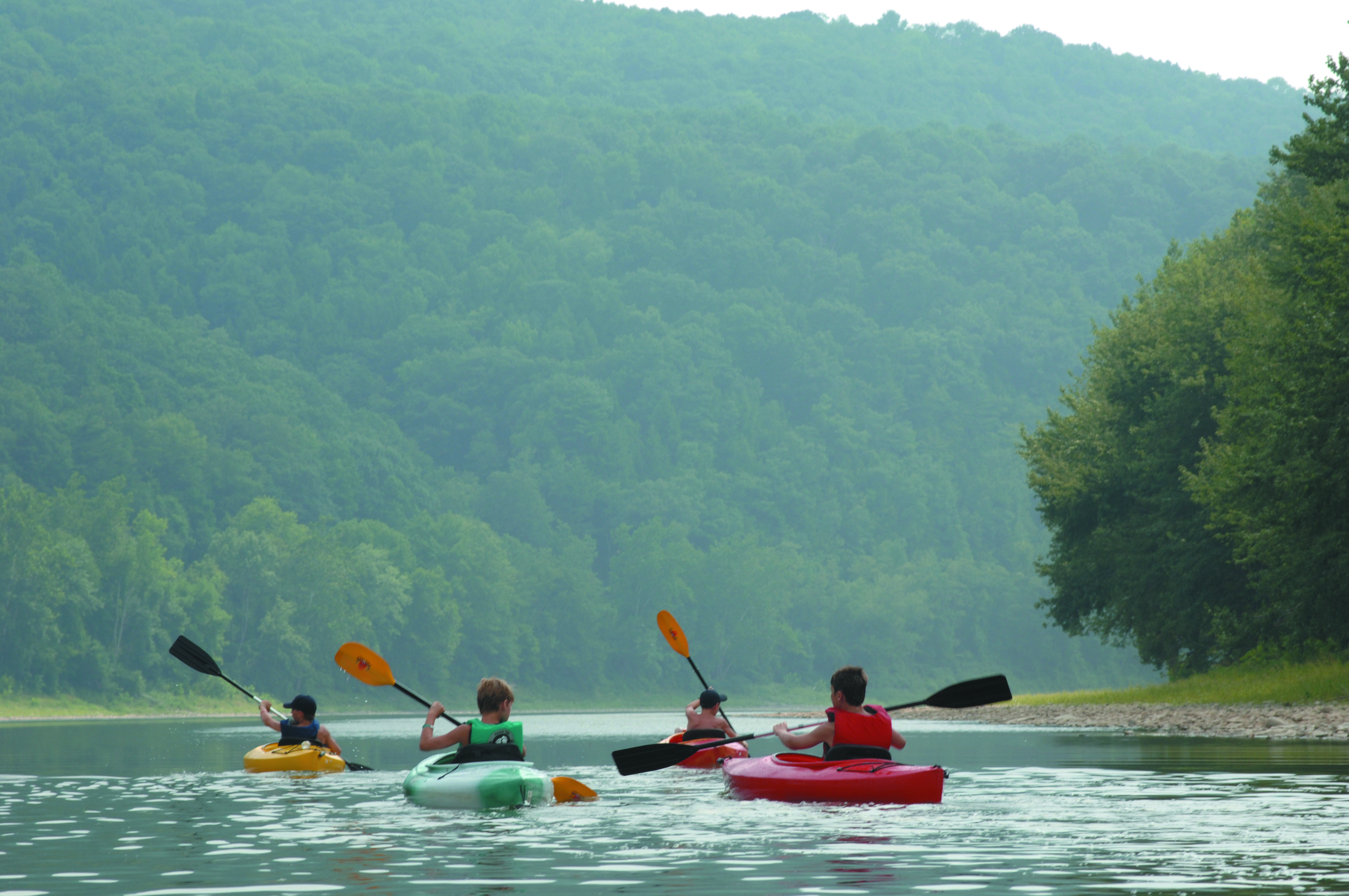 Four youngsters paddle kayaks on calm waters of the Susquehanna River