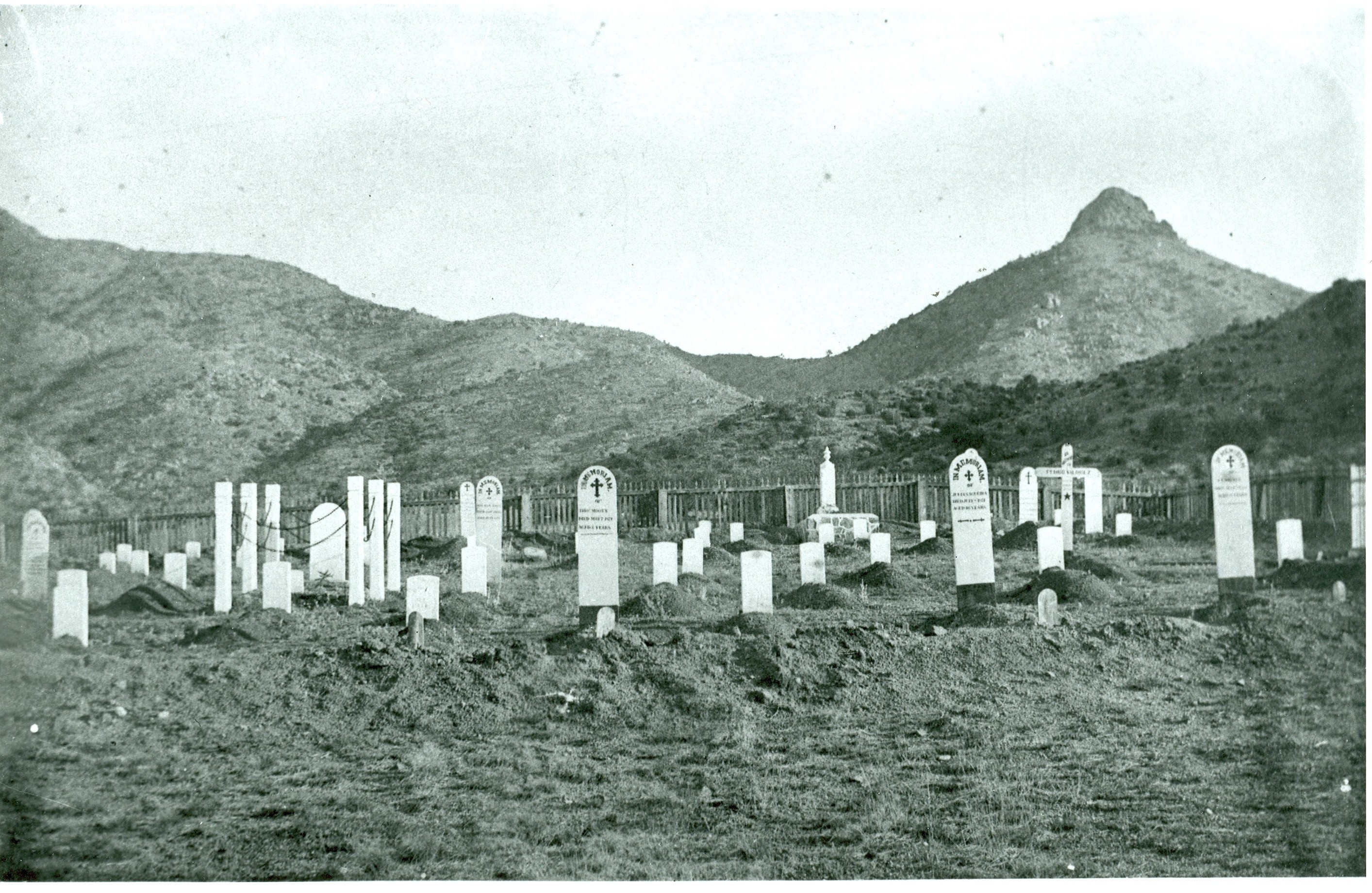 Black and white photo of white tombstones in a cemetery, mountains in the background