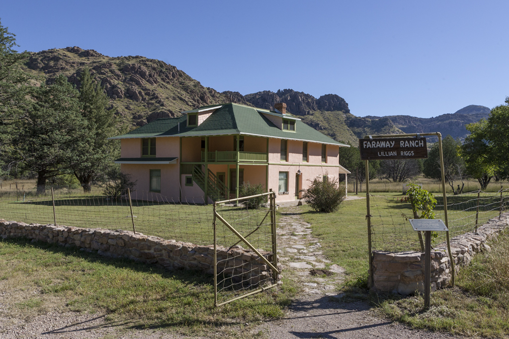 A ranch house in a green field surrounds by low mountains