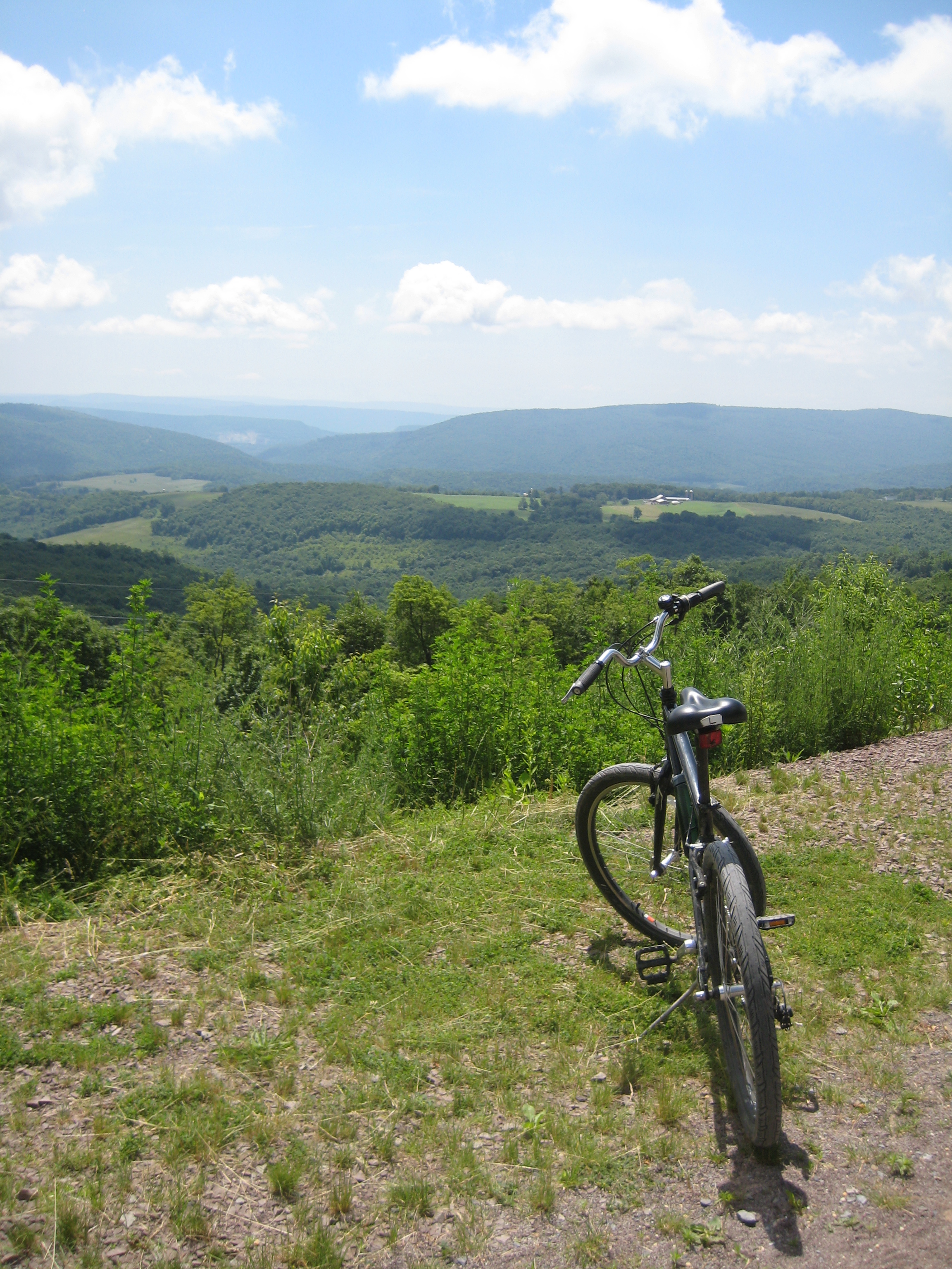 A bicycle sits on a bright summer day overlooking the rolling mountains in the distance.