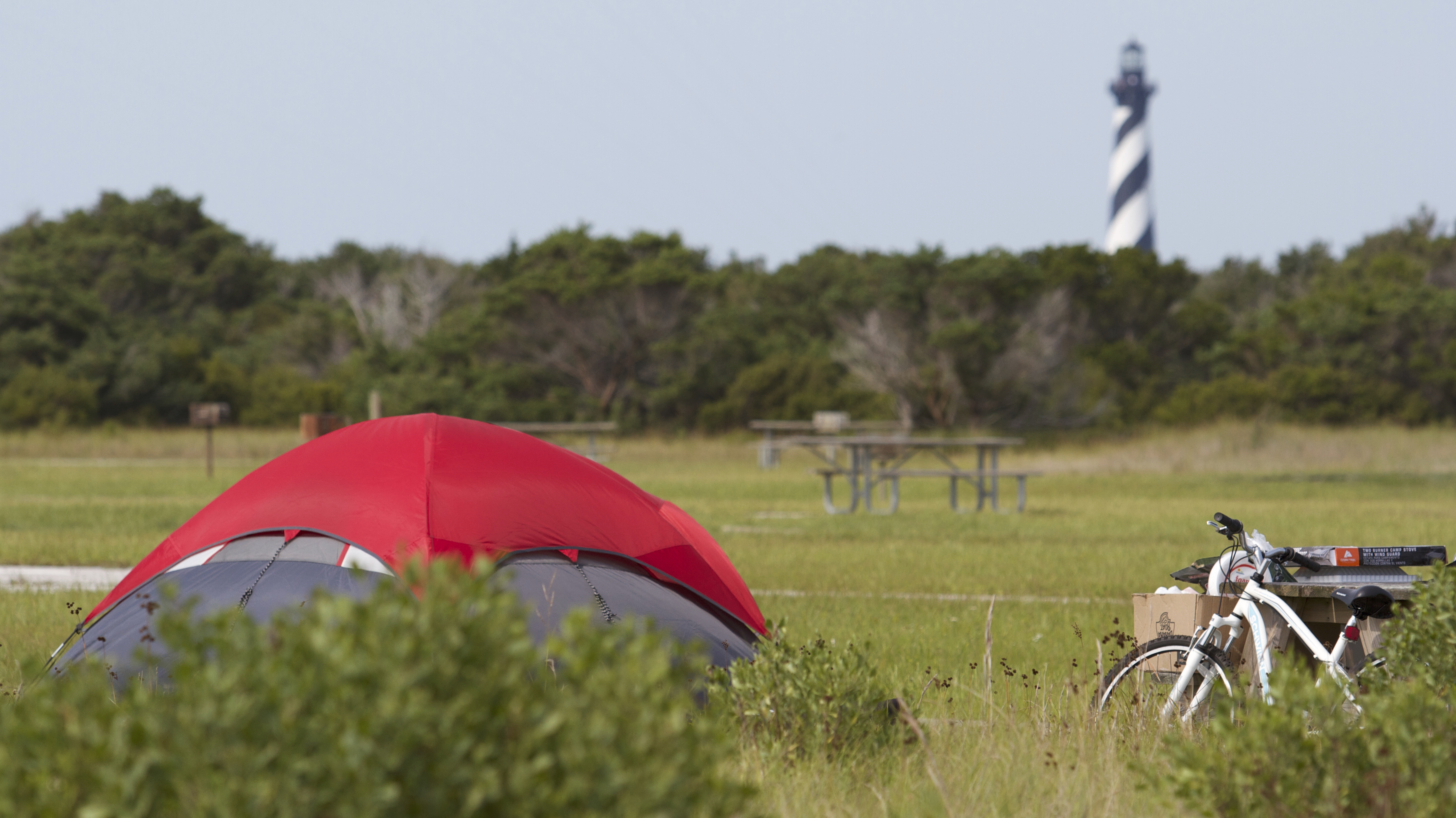 Red tent and bicycle at a camp site with the Cape Hatteras Lighthouse in the background.