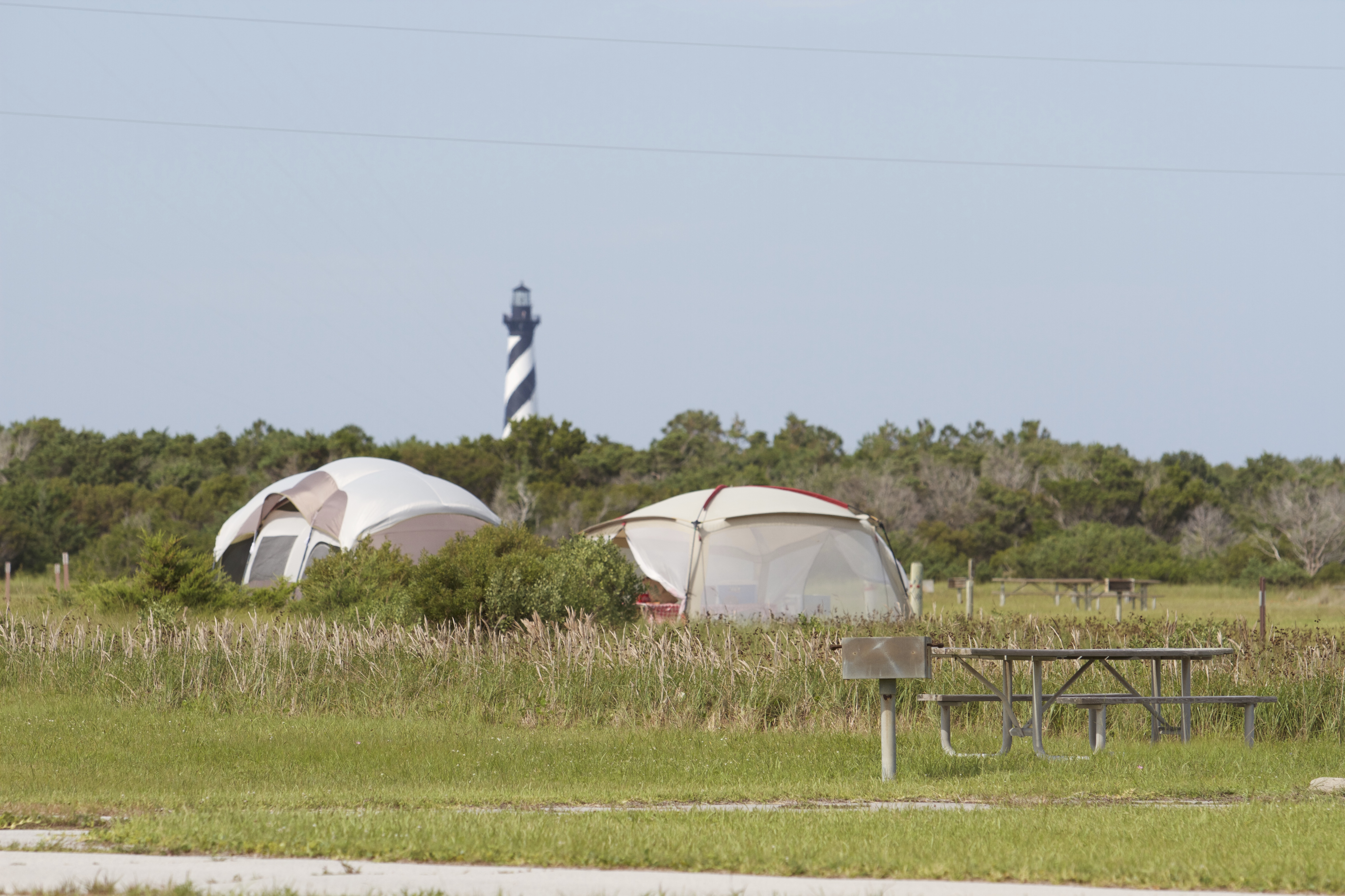 Two tents and the Cape Hatteras Lighthouse visible behind a grassy camp site.