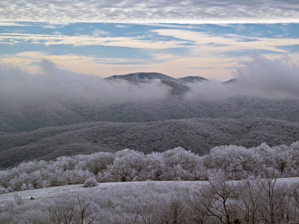A snowy winter view from the A.T. overlooking snowy mountains and clouds in the distance.