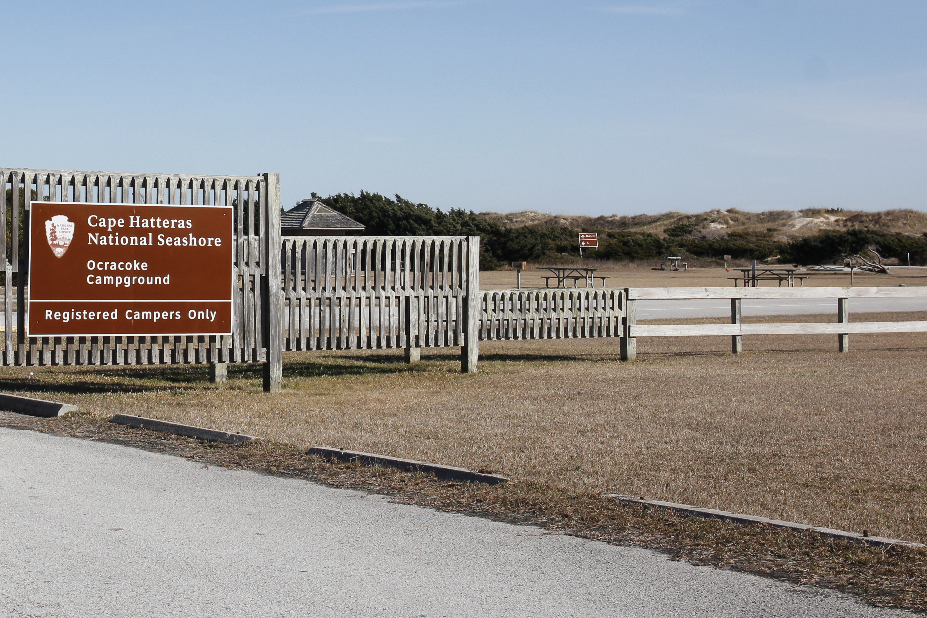 Brown entrance sign and wooden fence at Ocracoke Campground.