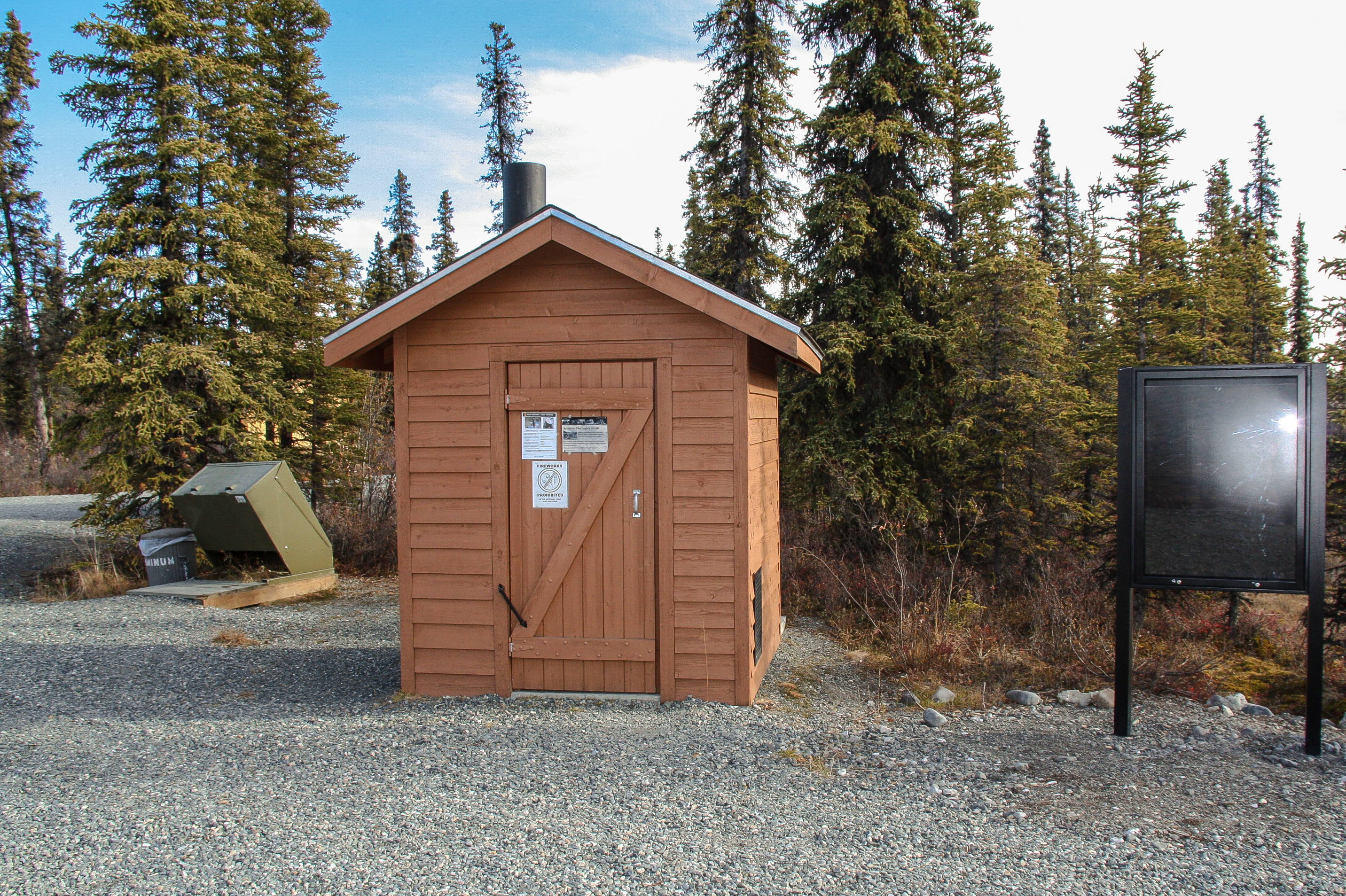 Outside view of vault toilet next to bear-proof trash canisters with forest in the background