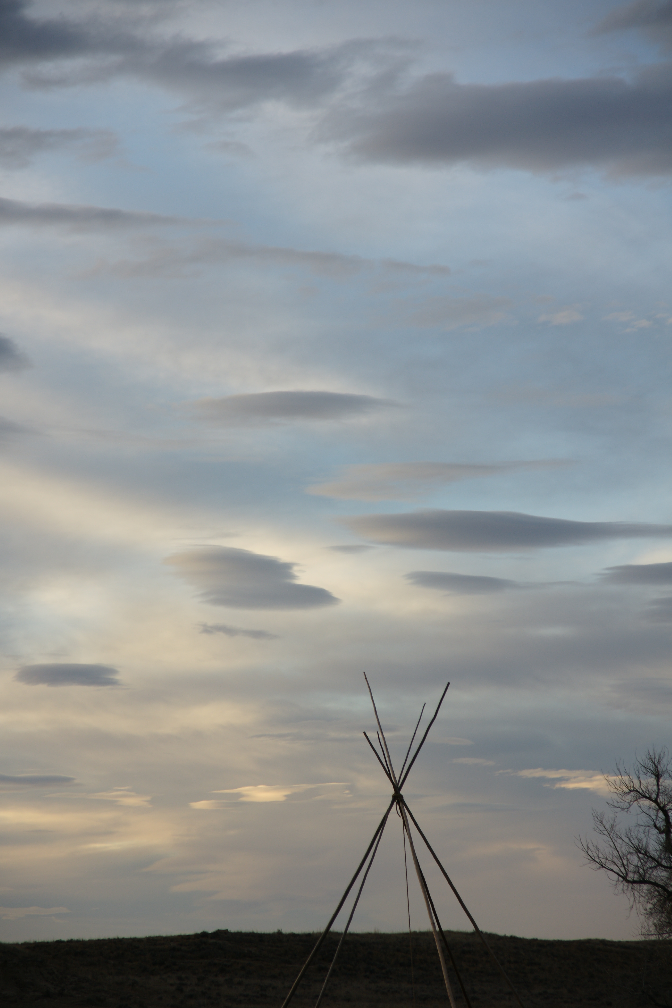 A tipi frame is silhouetted by the evening sky.