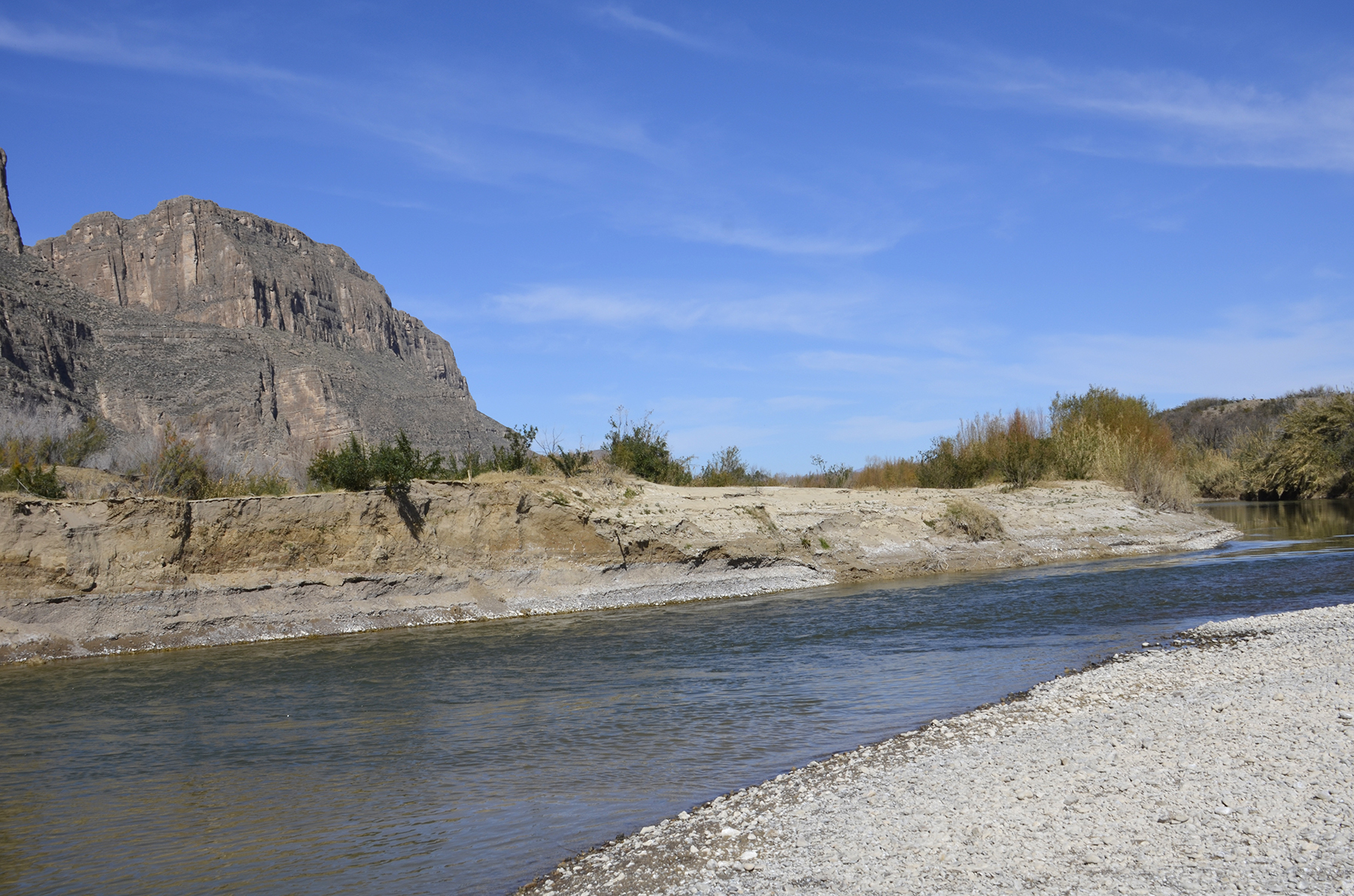 A desert river with a rugged landscape of cliff faces and hills in the background.