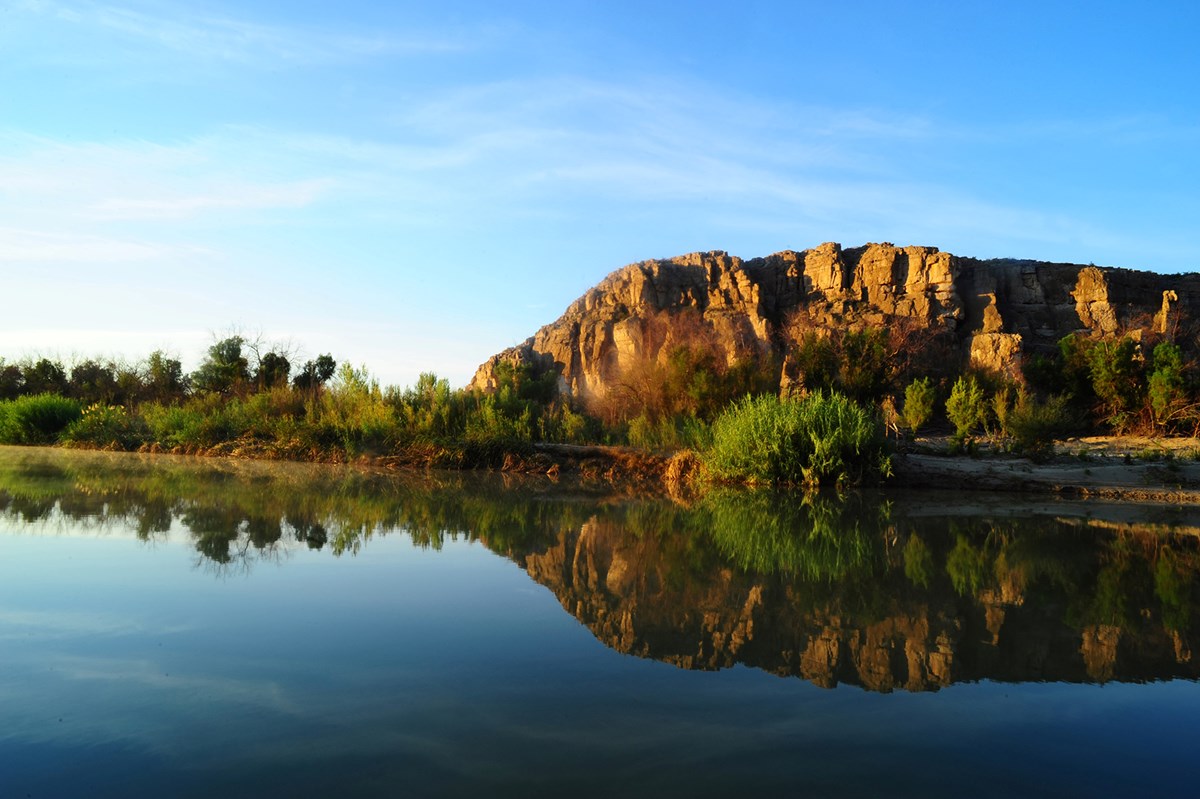 A desert river with a tree lined bank in the background.