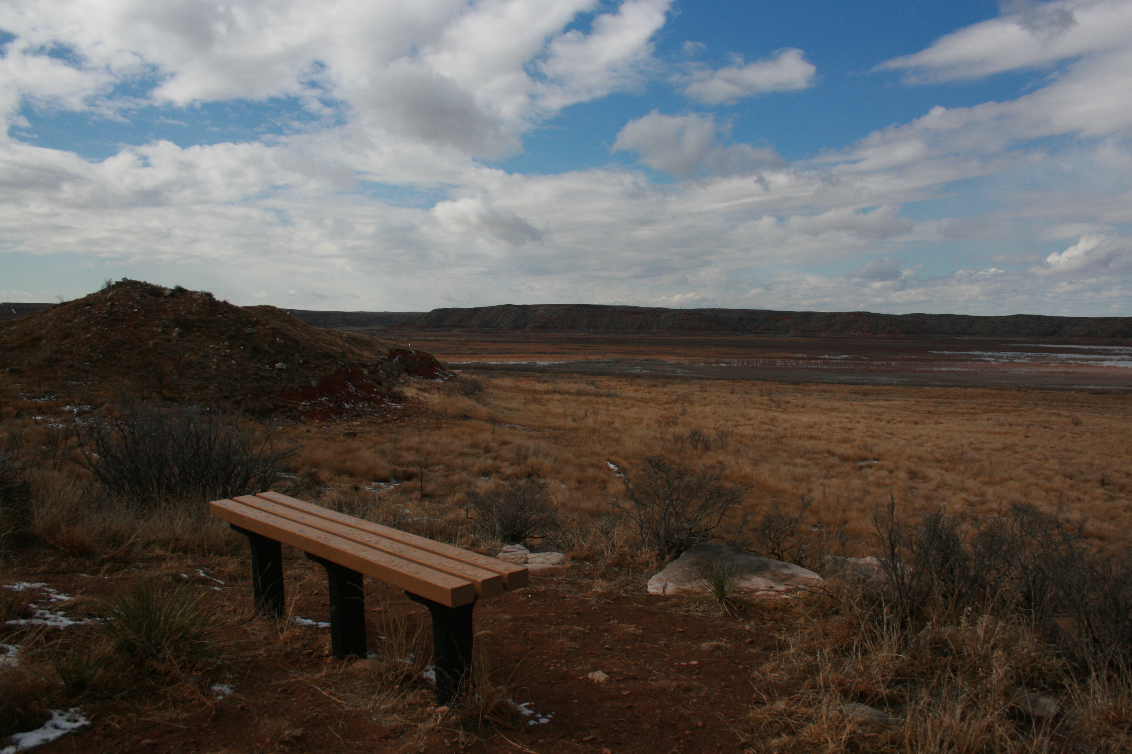 A bench on the Harbor Bay Trail, overlooking Lake Meredith. The sky is blue with white clouds.