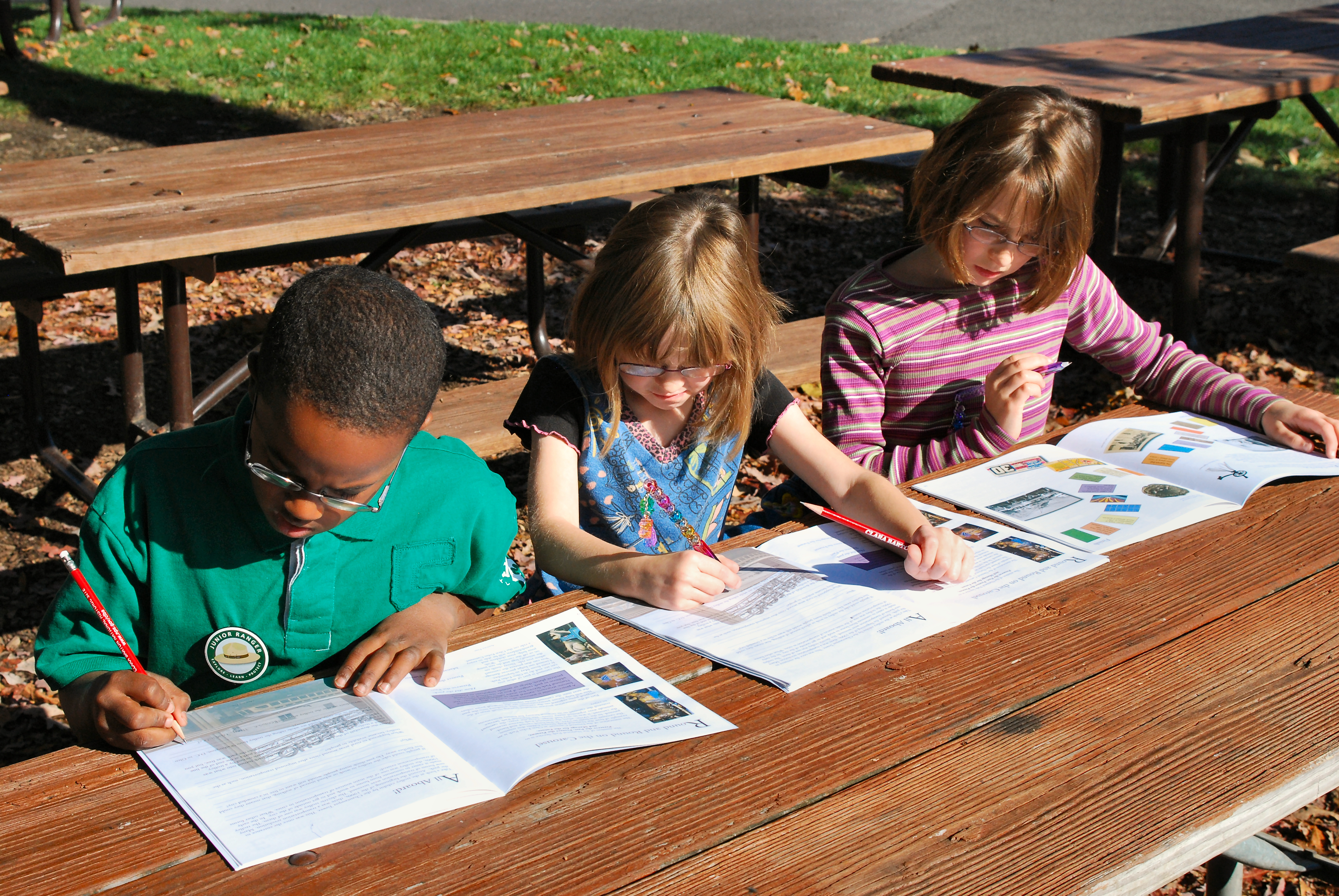 three children seated at a picnic table working on a Glen Echo Park Junior Ranger Booklet.
