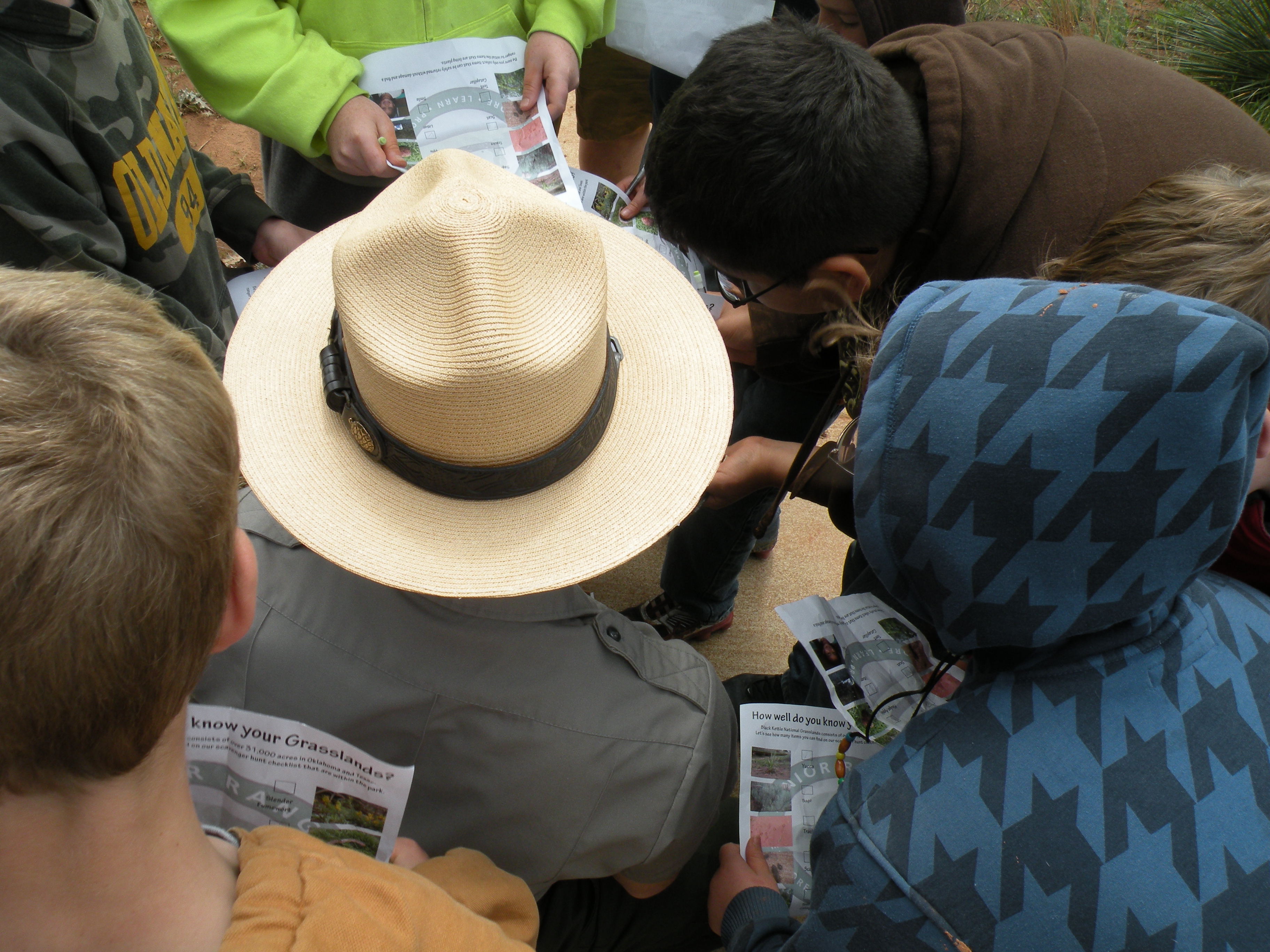 A Park Ranger knells down among Junior Rangers so only his hat shows within the crowd of children.