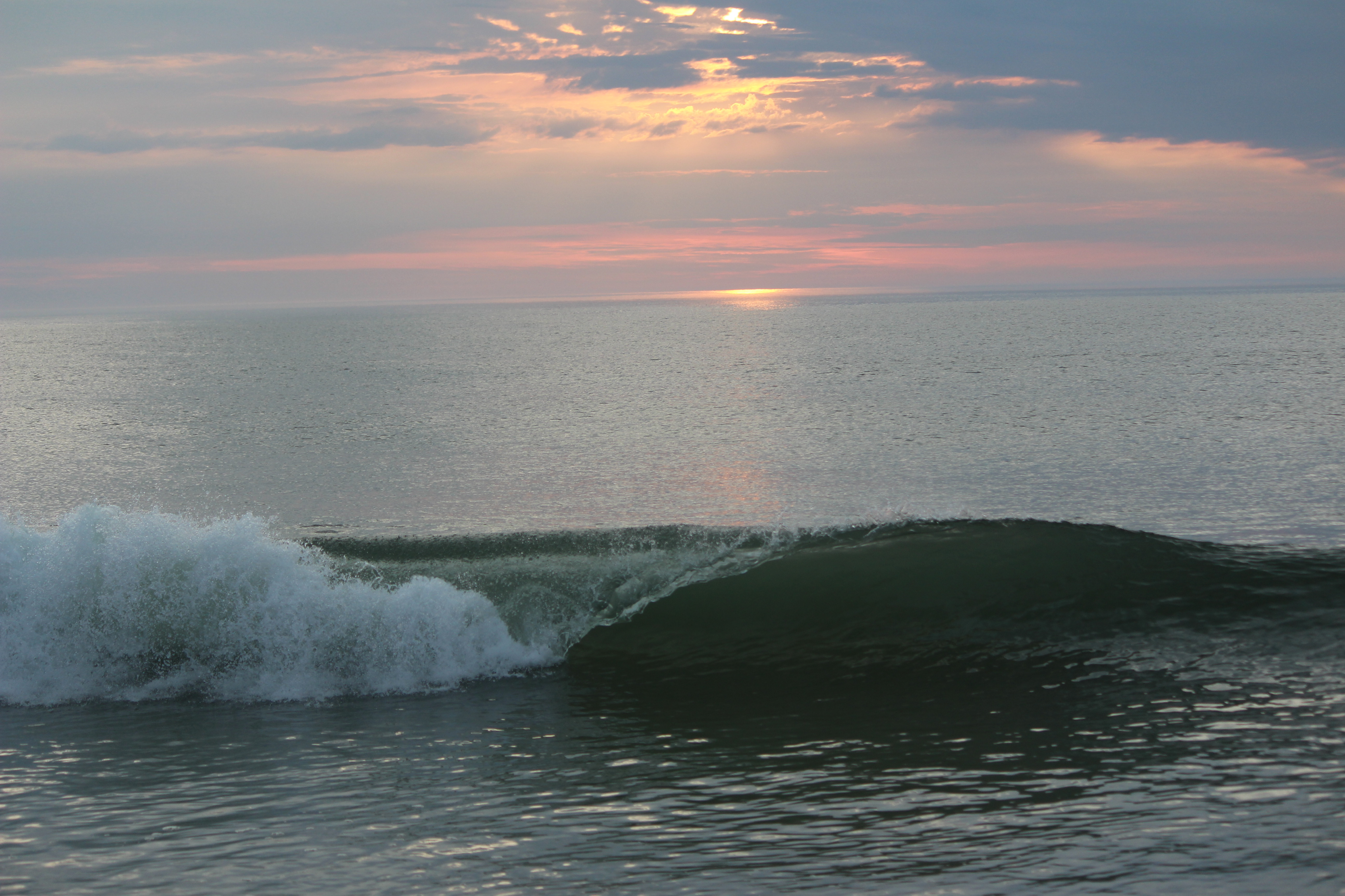 A curling wave breaks against the backdrop of a pink sunrise.