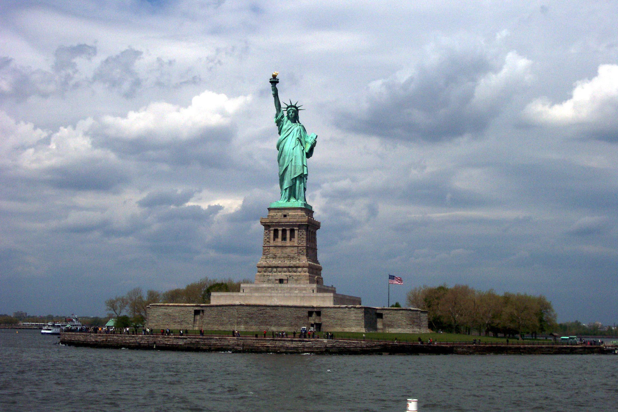 Patina green statue atop her pedestal on Liberty Island; grey cloudy sky in the distance