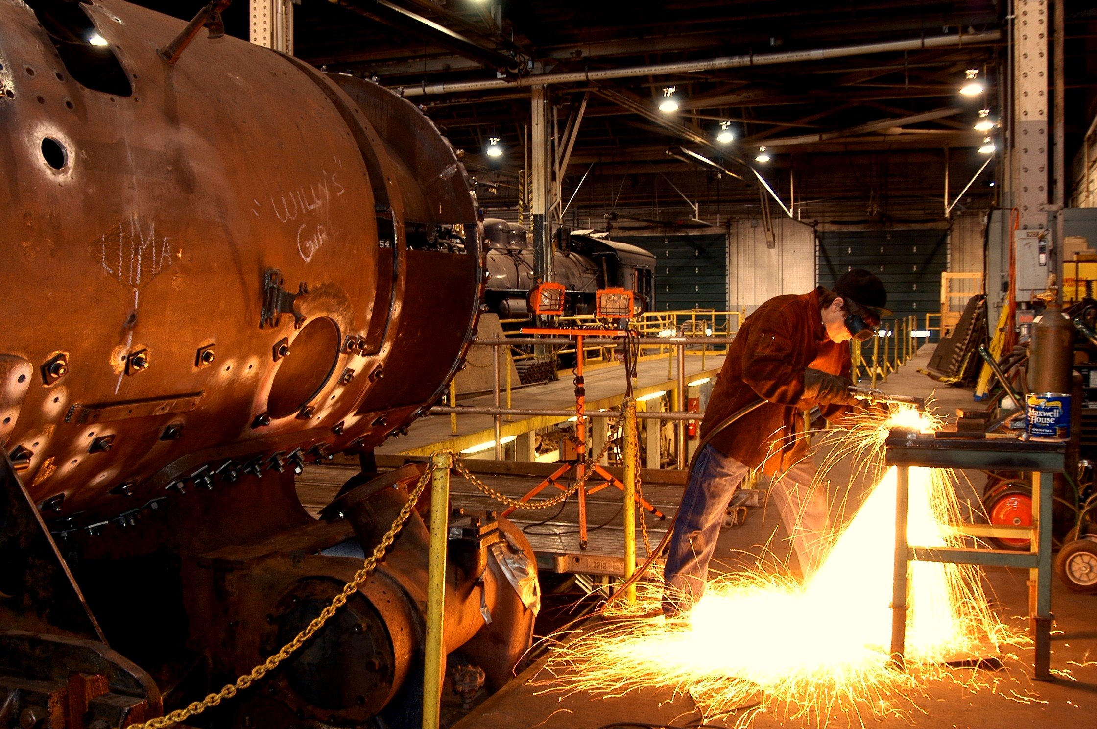 A mechanic grinds metal in the Locomotive Shop causing sparks to fly towards ground.