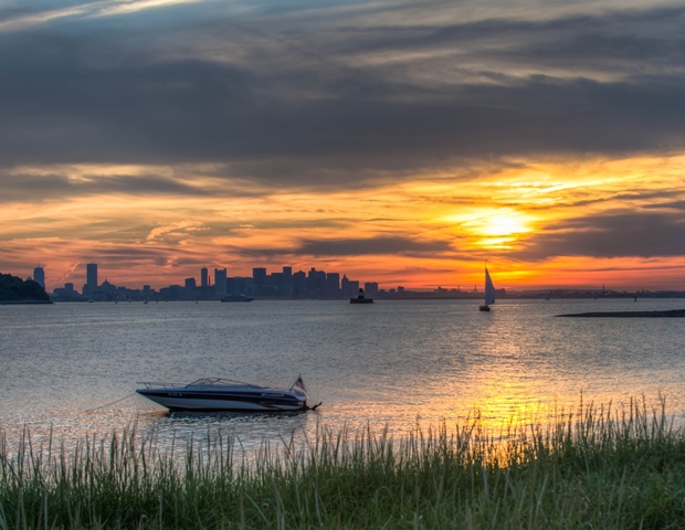An image of the sun setting over the Boston skyline from the Islands