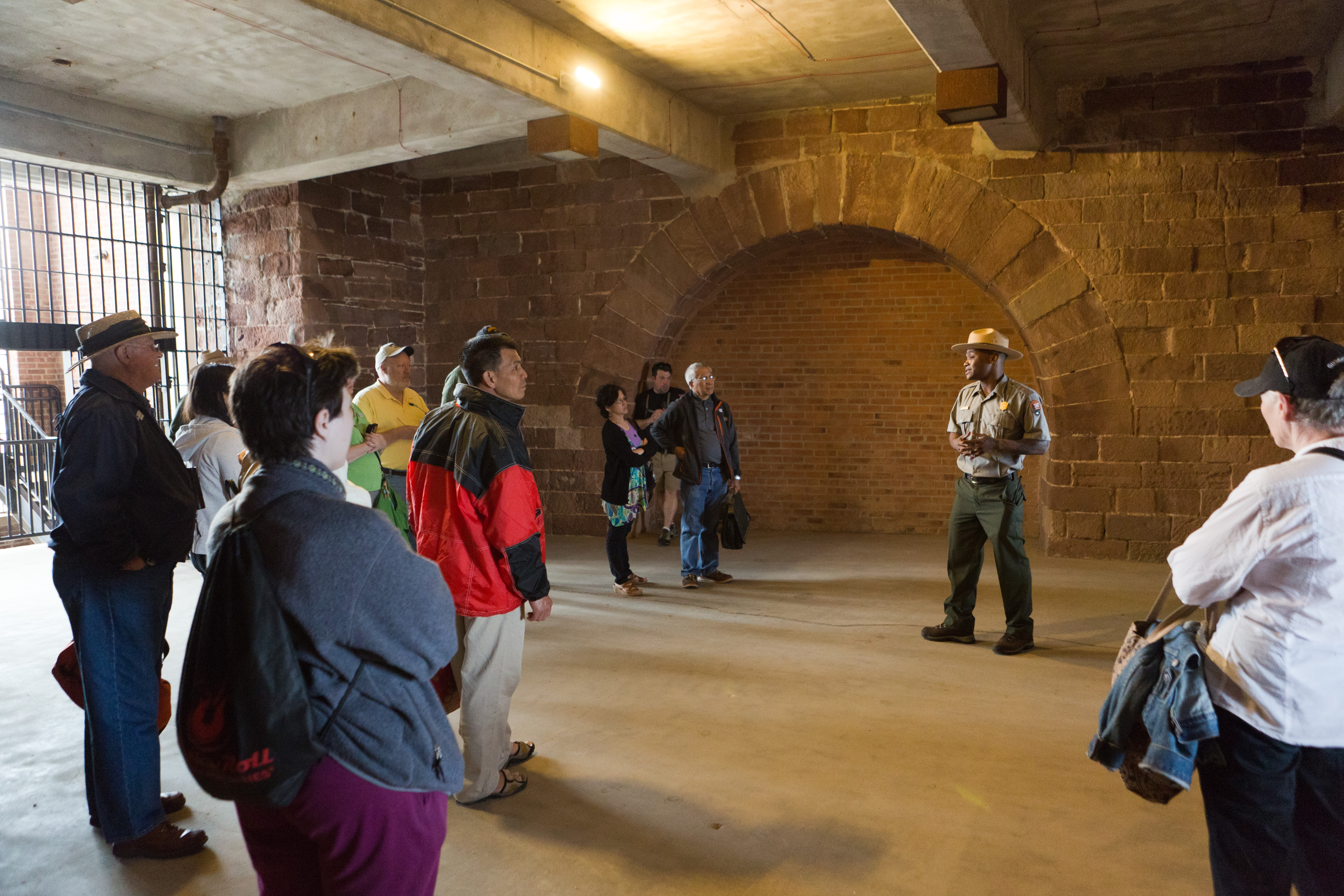 A park ranger talking to a group of visitors inside a large stone room in a fort.